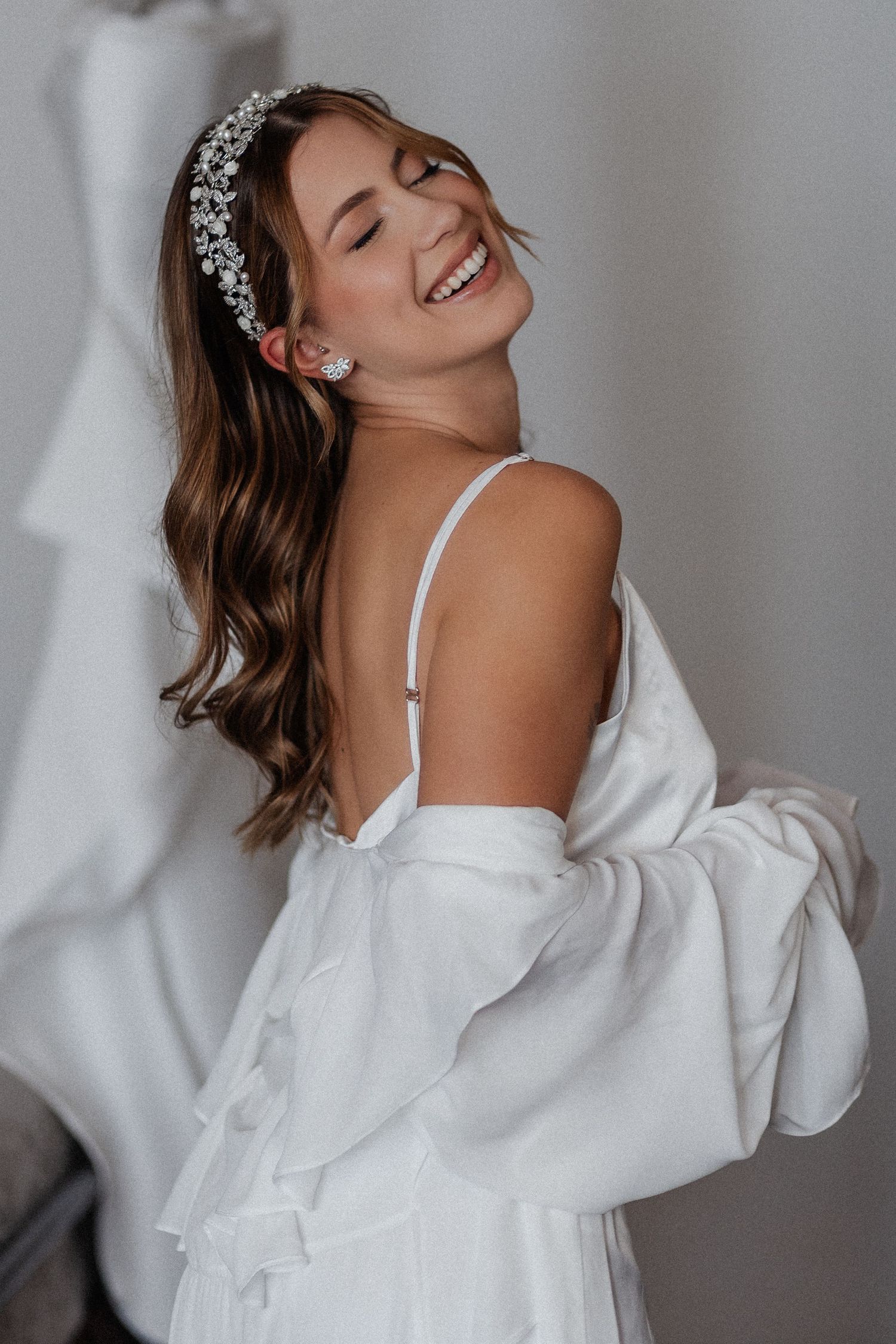 Portrait of someone smiling and wearing a delicate bridal headpiece with an elegant white off-shoulder gown.