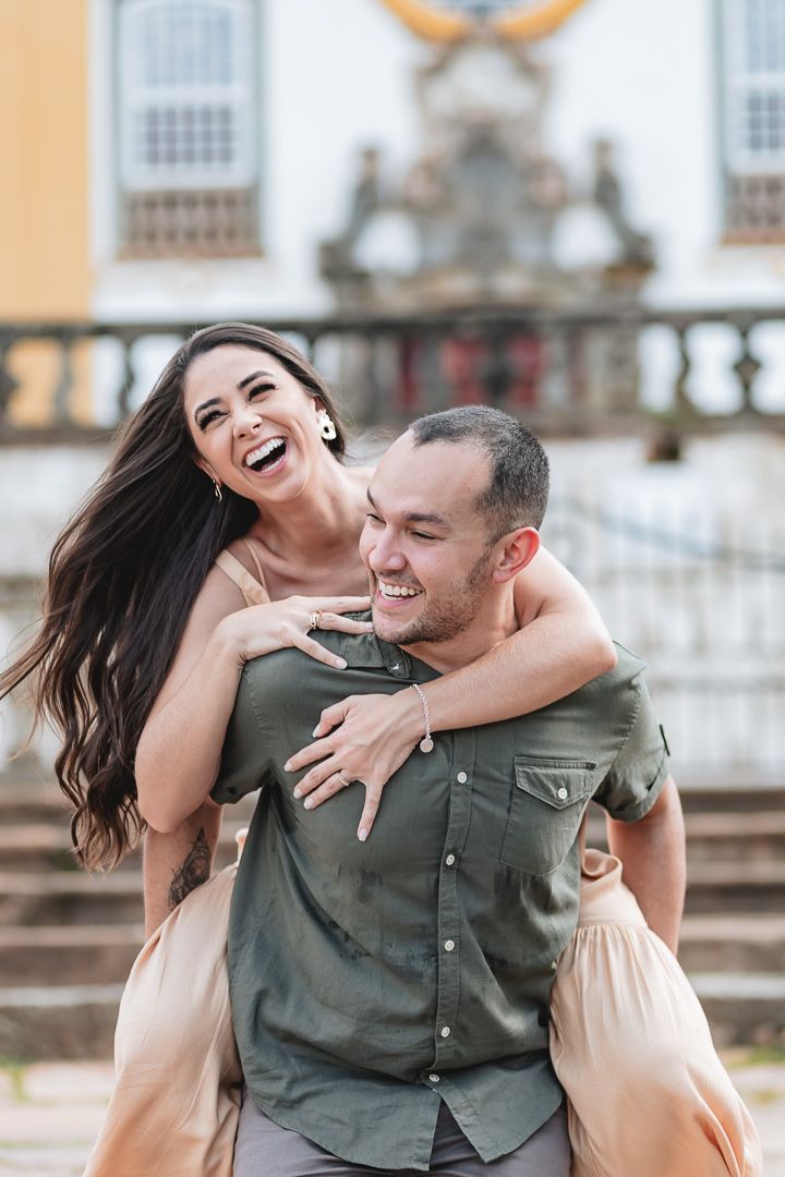 A joyful couple laughs together during a playful piggyback moment on stone steps outside a historic building.