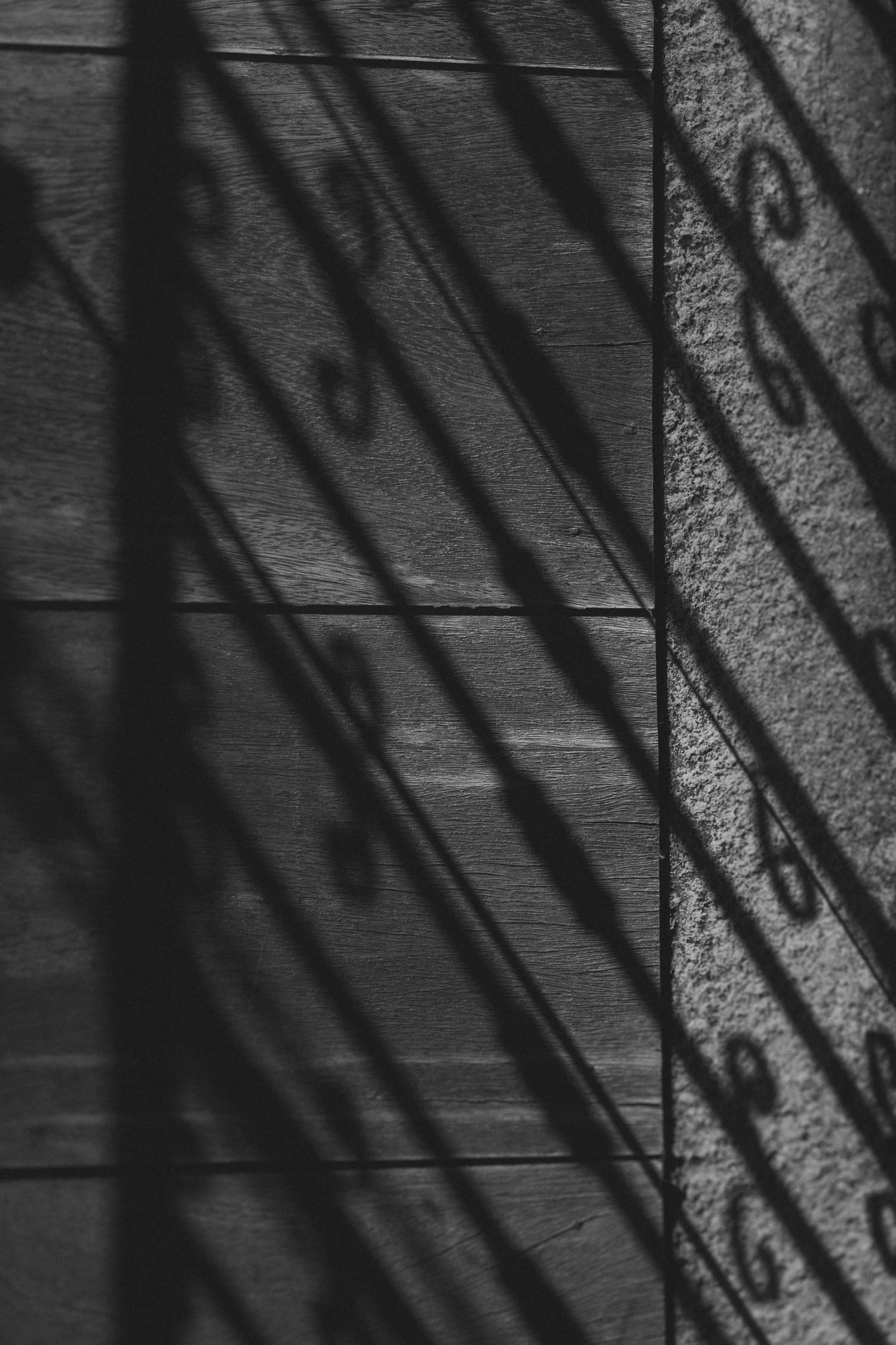 Dramatic diagonal shadows cast by sunlight create a stark pattern of lines across a textured wood surface.