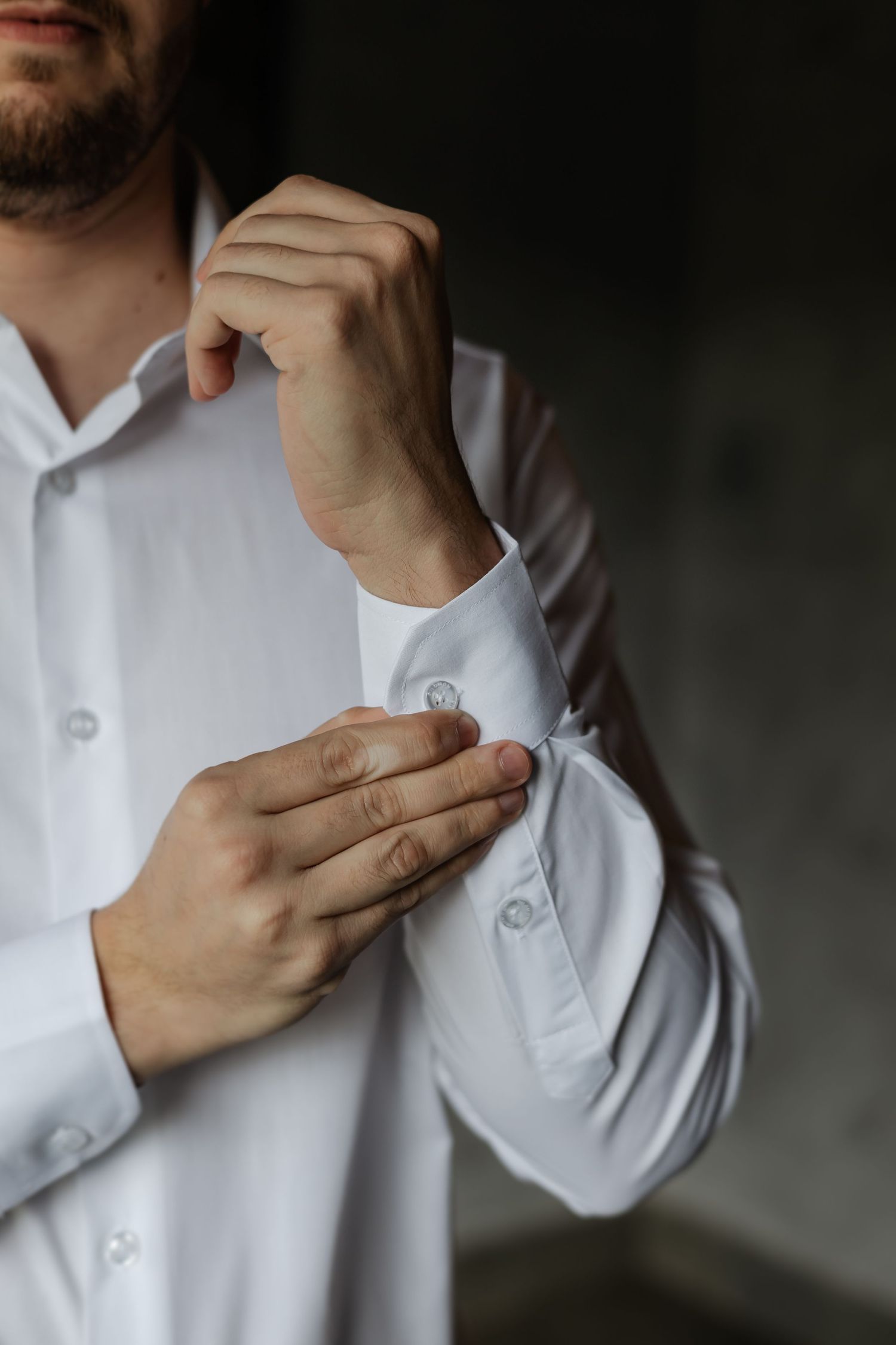 Someone adjusting the cuff of a crisp white dress shirt in a moody lighting setting.