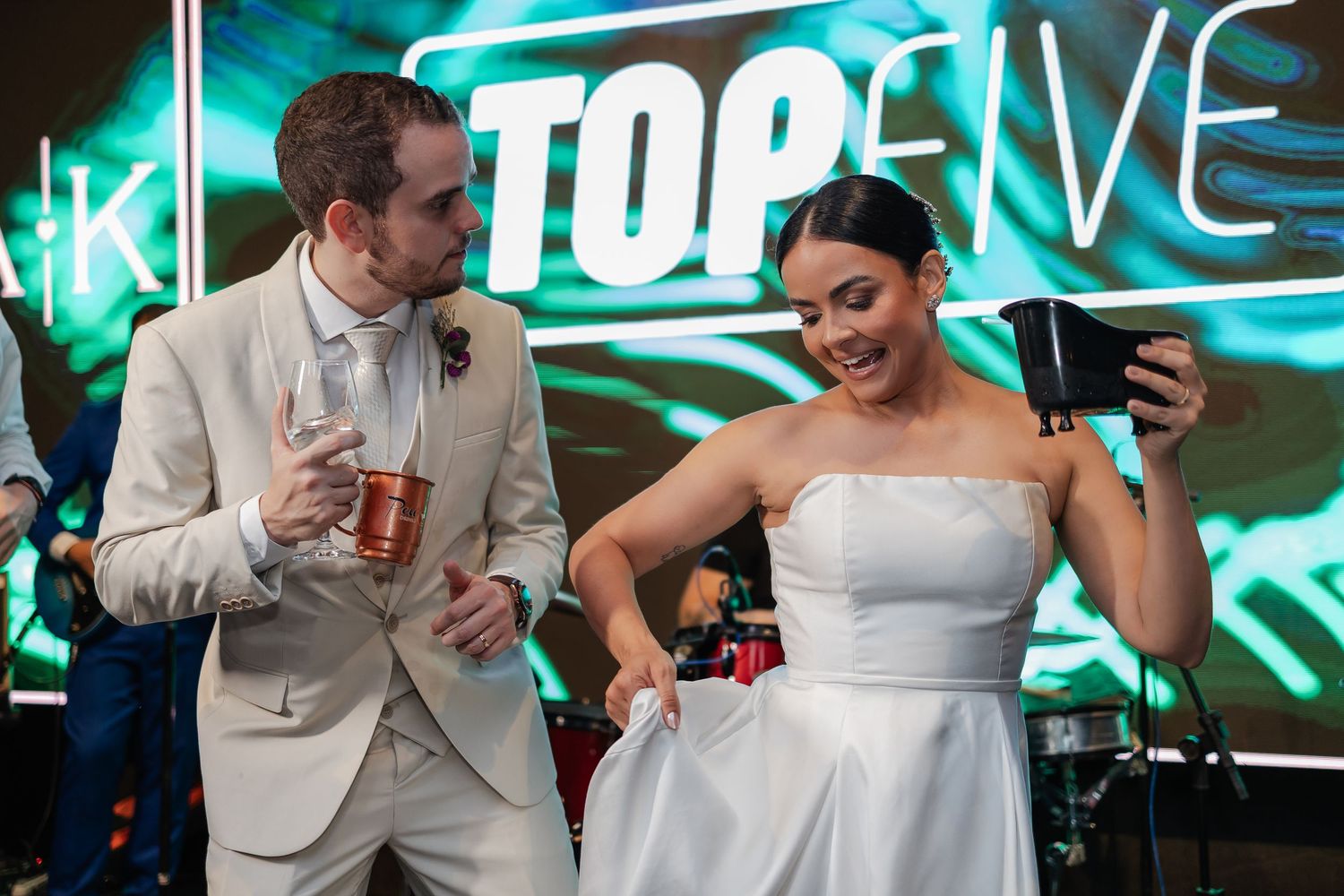 A couple shares a candid moment on their wedding day, with the bride in white dress and groom in light suit under neon signage.