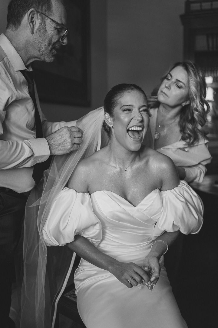 A joyful moment captured in black and white as a bride laughs while getting ready with her wedding party.