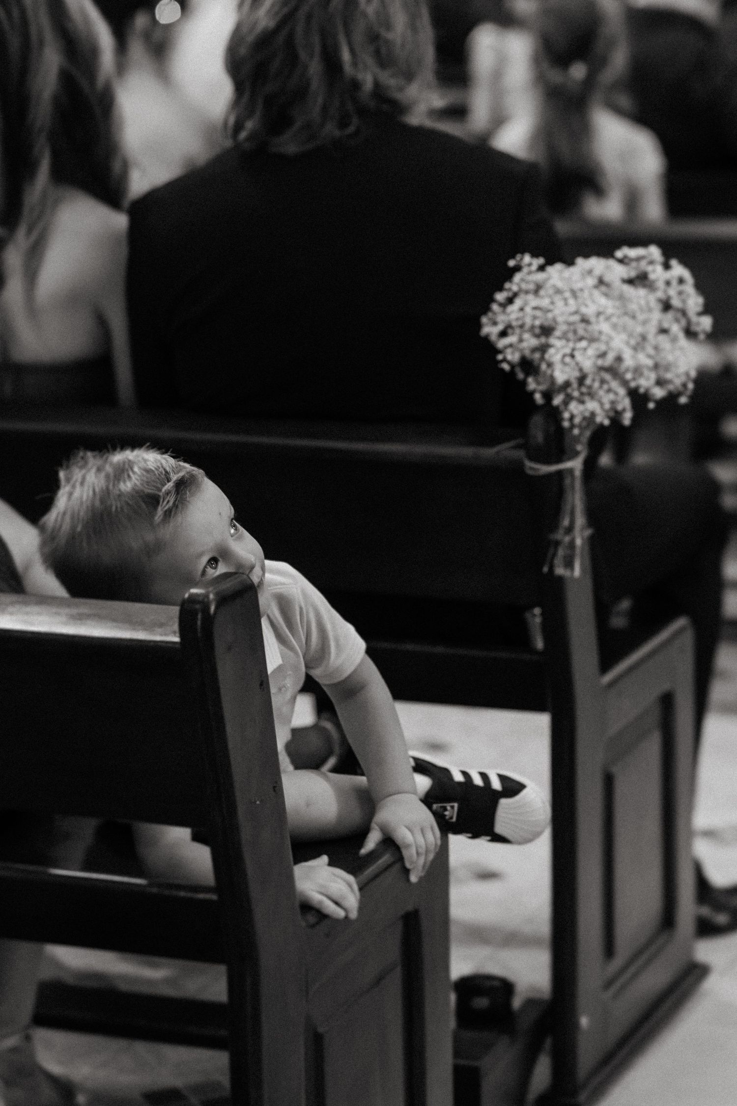 Black and white wedding photo showing delicate floral arrangements decorating wooden church pews.