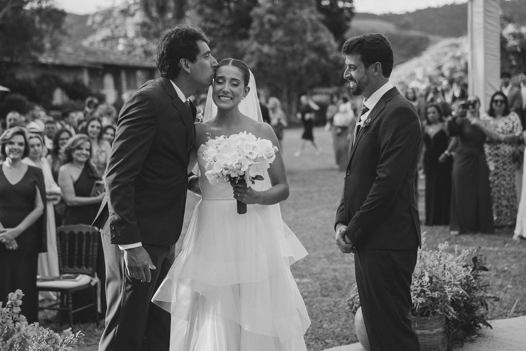 A joyful black and white wedding ceremony scene outdoors with a bride in a white dress holding a bouquet.