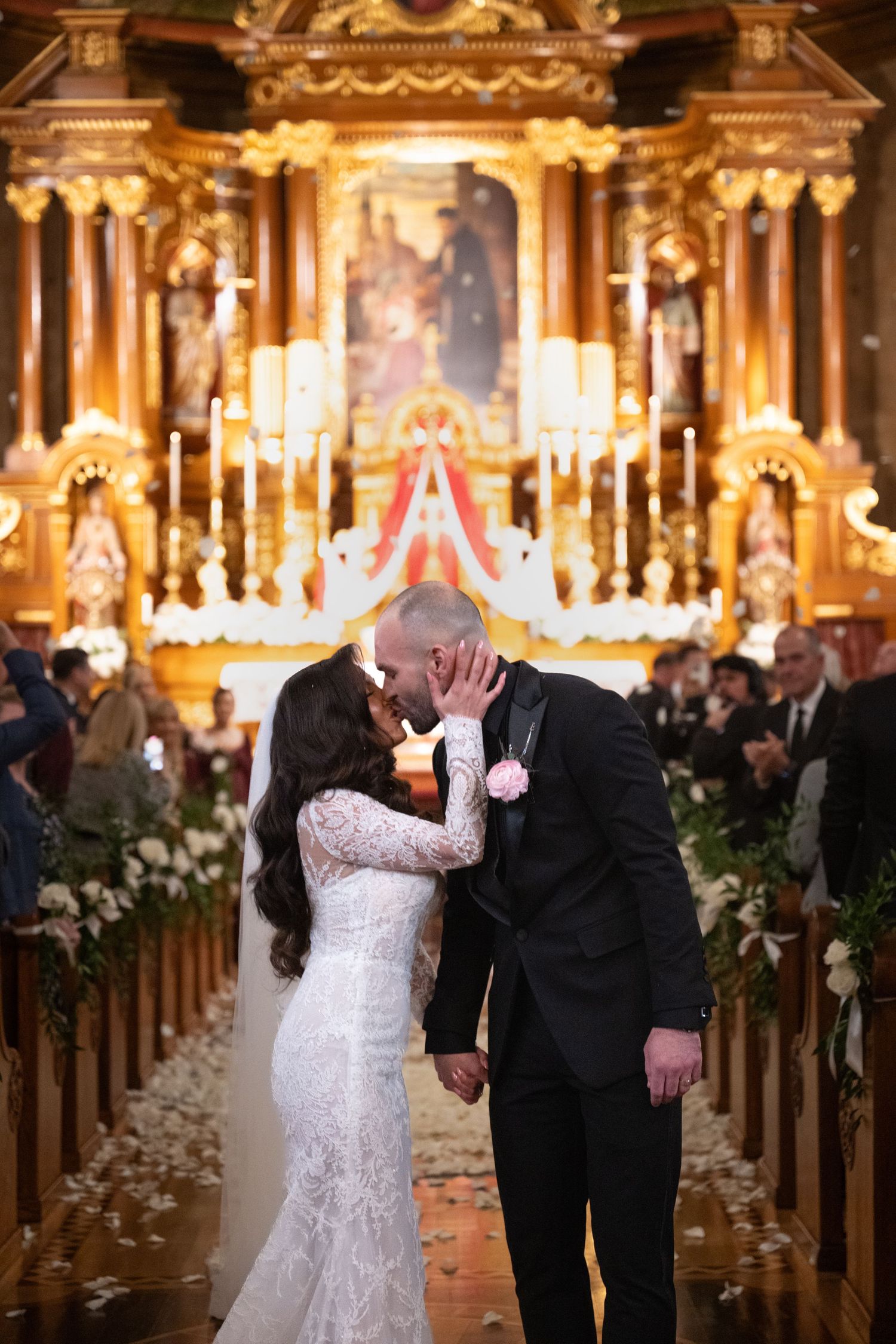 A romantic wedding ceremony in an ornate church with glowing candles and floral decorations lining the aisle.