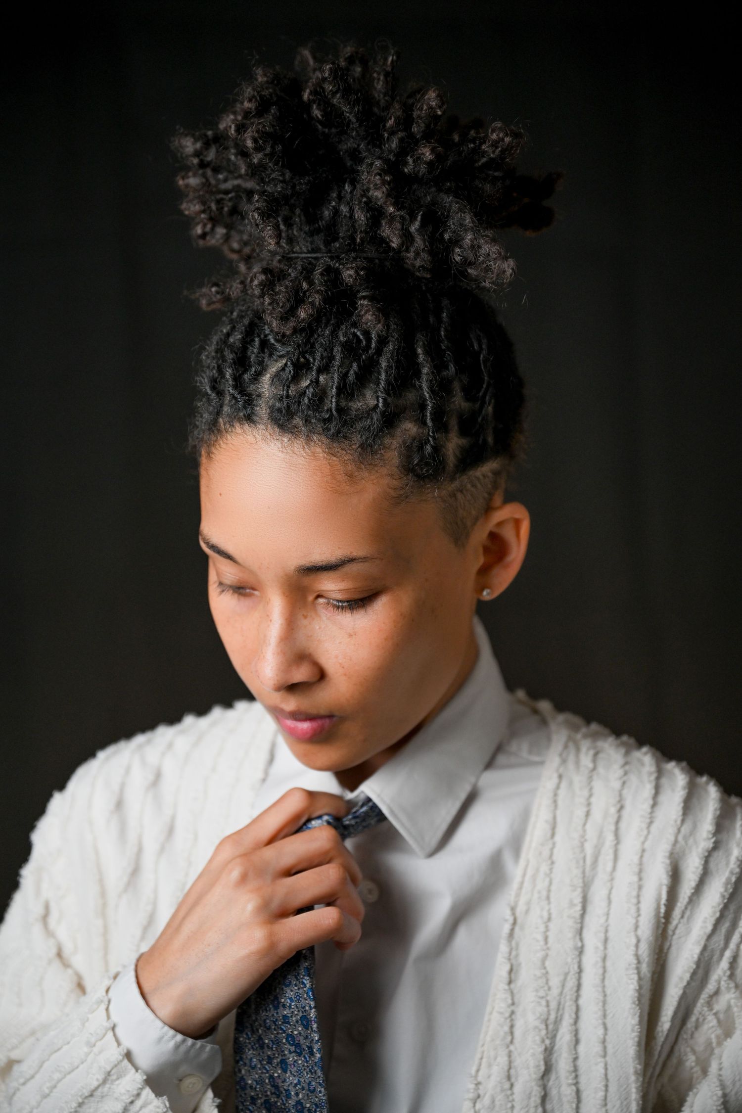 Thoughtful portrait series showing someone in white cable knit sweater against dark background.
