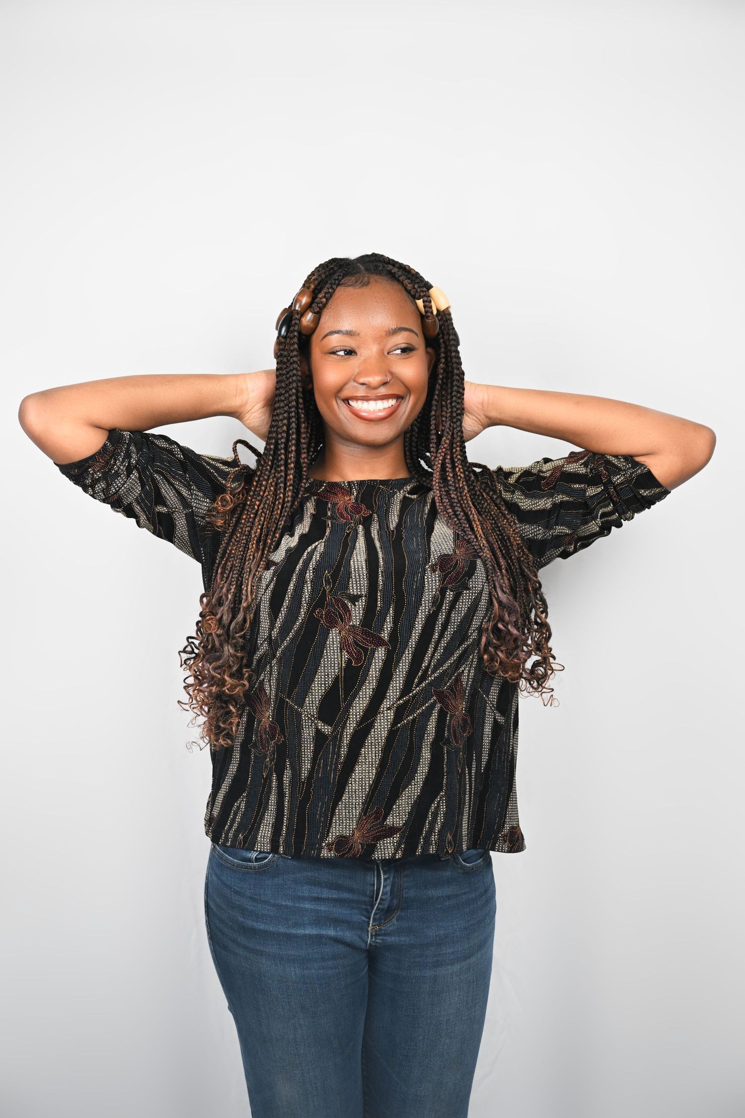 Joyful pose with hands behind head showing off braided hairstyle and striped top.