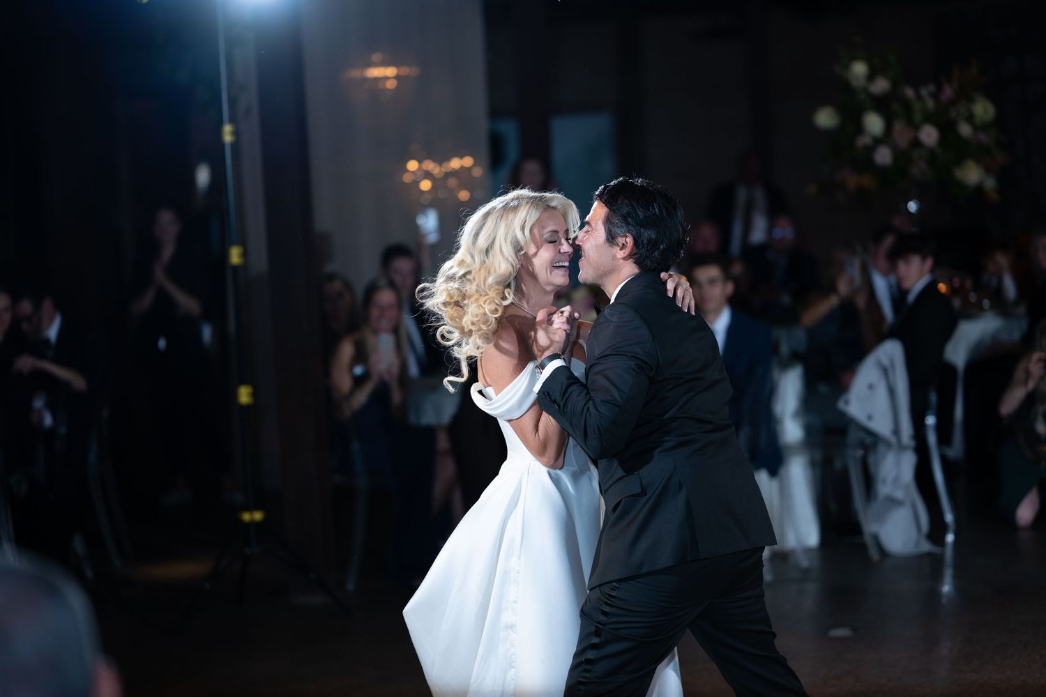 Two people sharing an intimate dance moment under dramatic lighting at what appears to be a wedding reception.