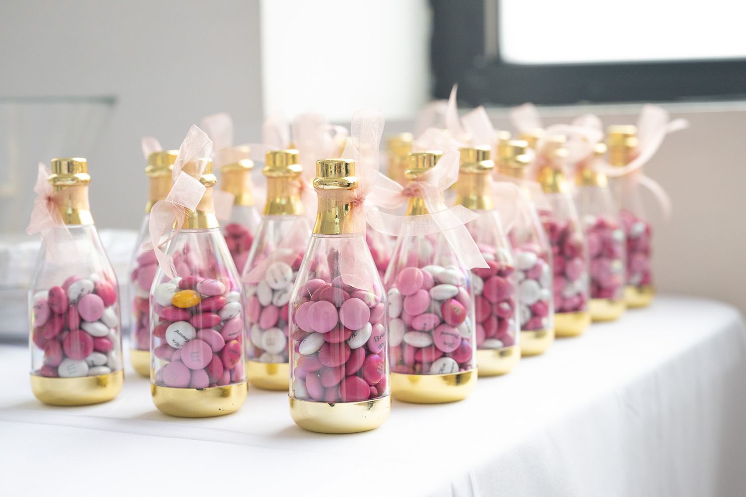 Decorative mini champagne bottles filled with pink petals lined up on a white surface.