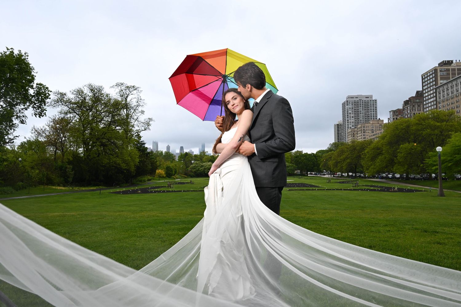 A couple poses with a colorful umbrella in a park during their wedding photoshoot.