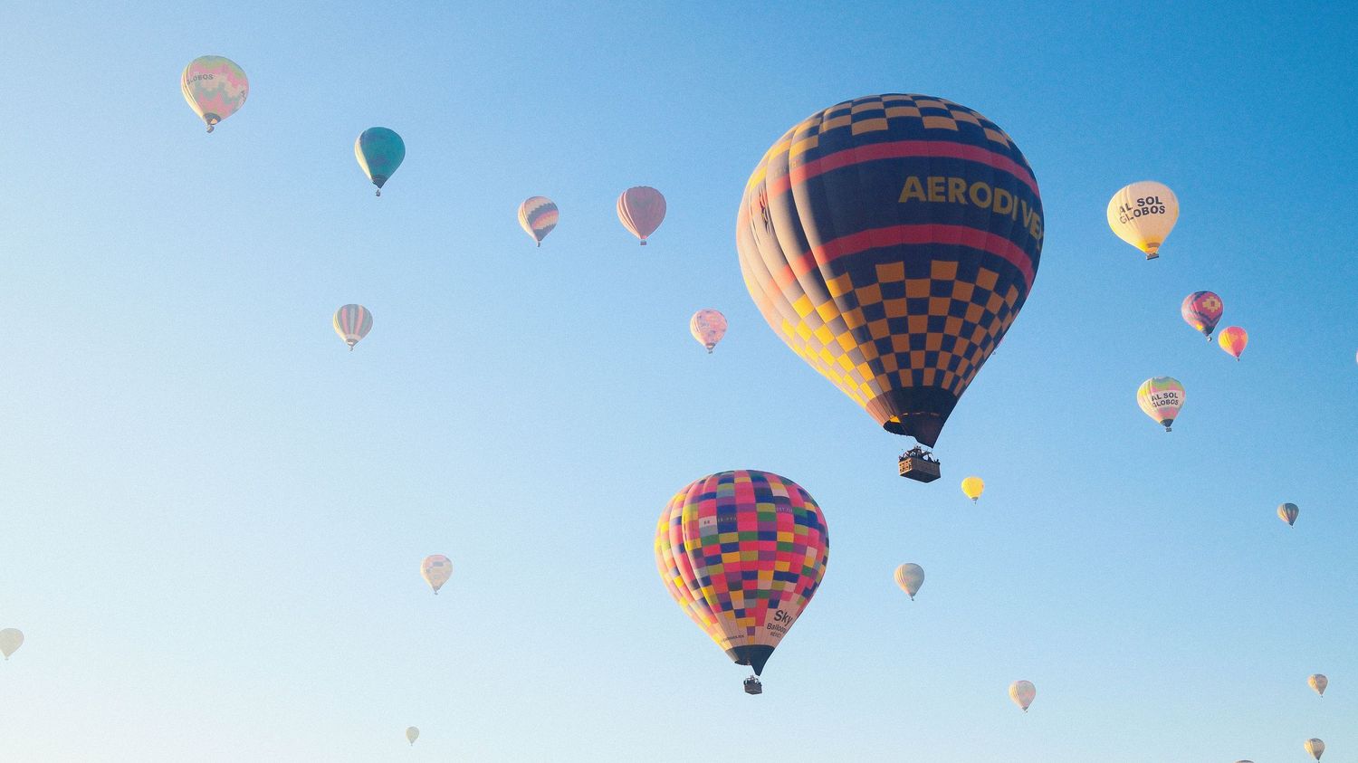 Colorful hot air balloons float against a bright blue sky during a festival or gathering.