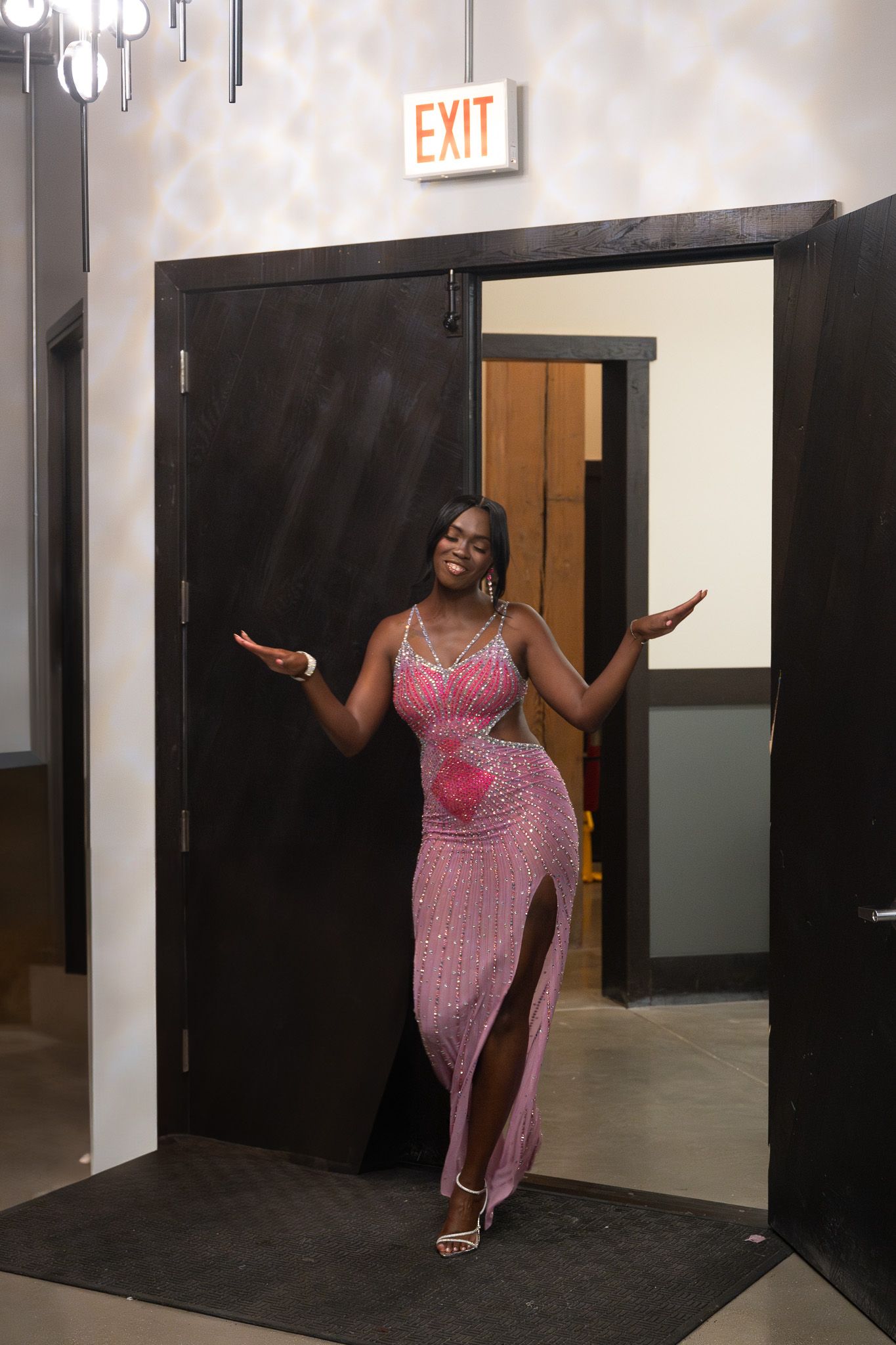 Person in sparkly pink dress poses dramatically in doorway near exit sign.