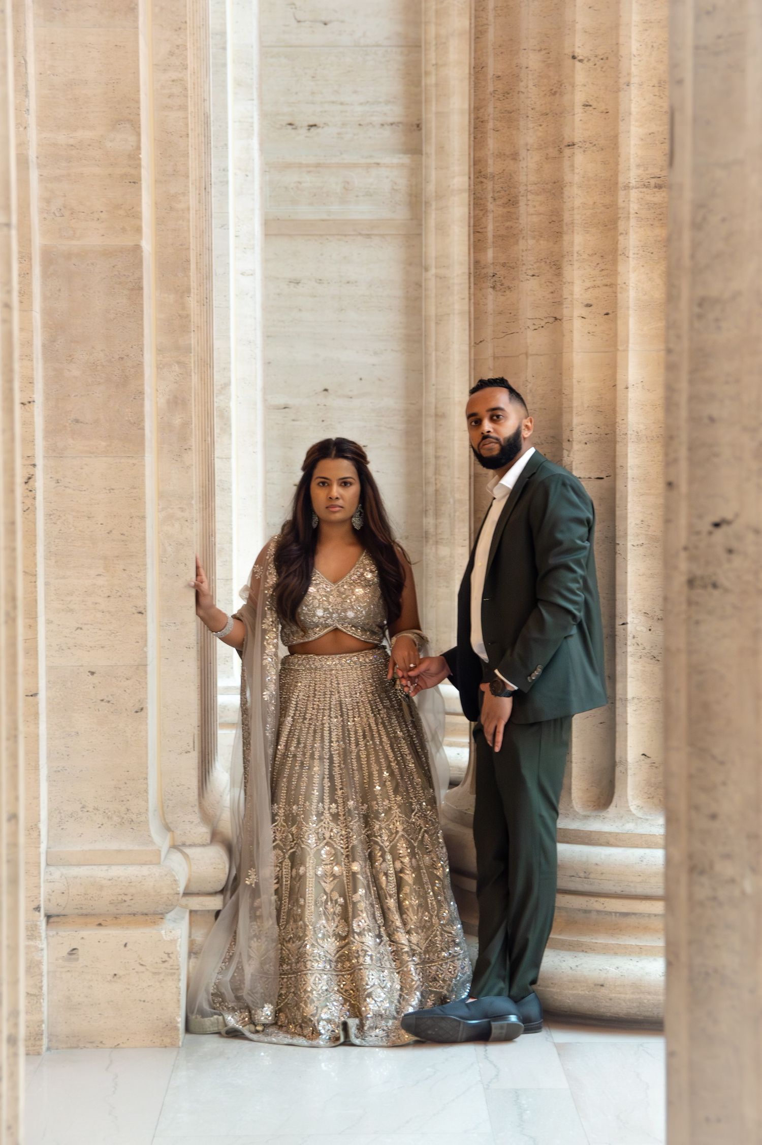 Elegant couple poses between classic columns wearing formal evening attire.