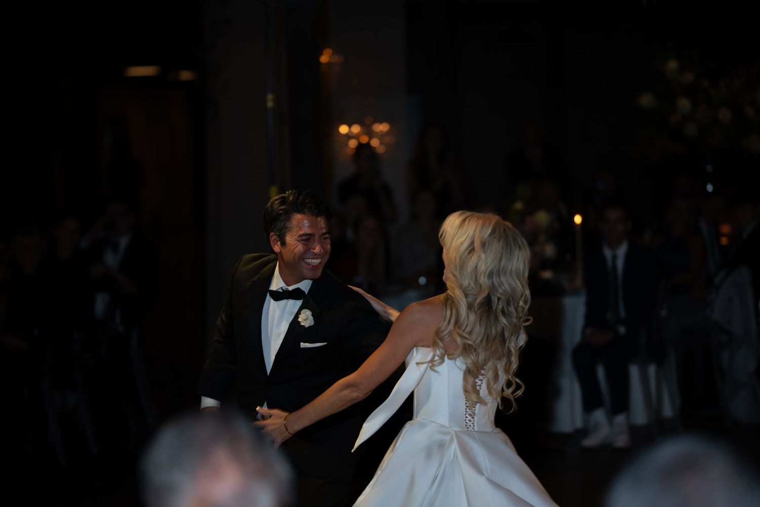 A couple shares their first dance at an evening wedding reception in a dimly lit ballroom.
