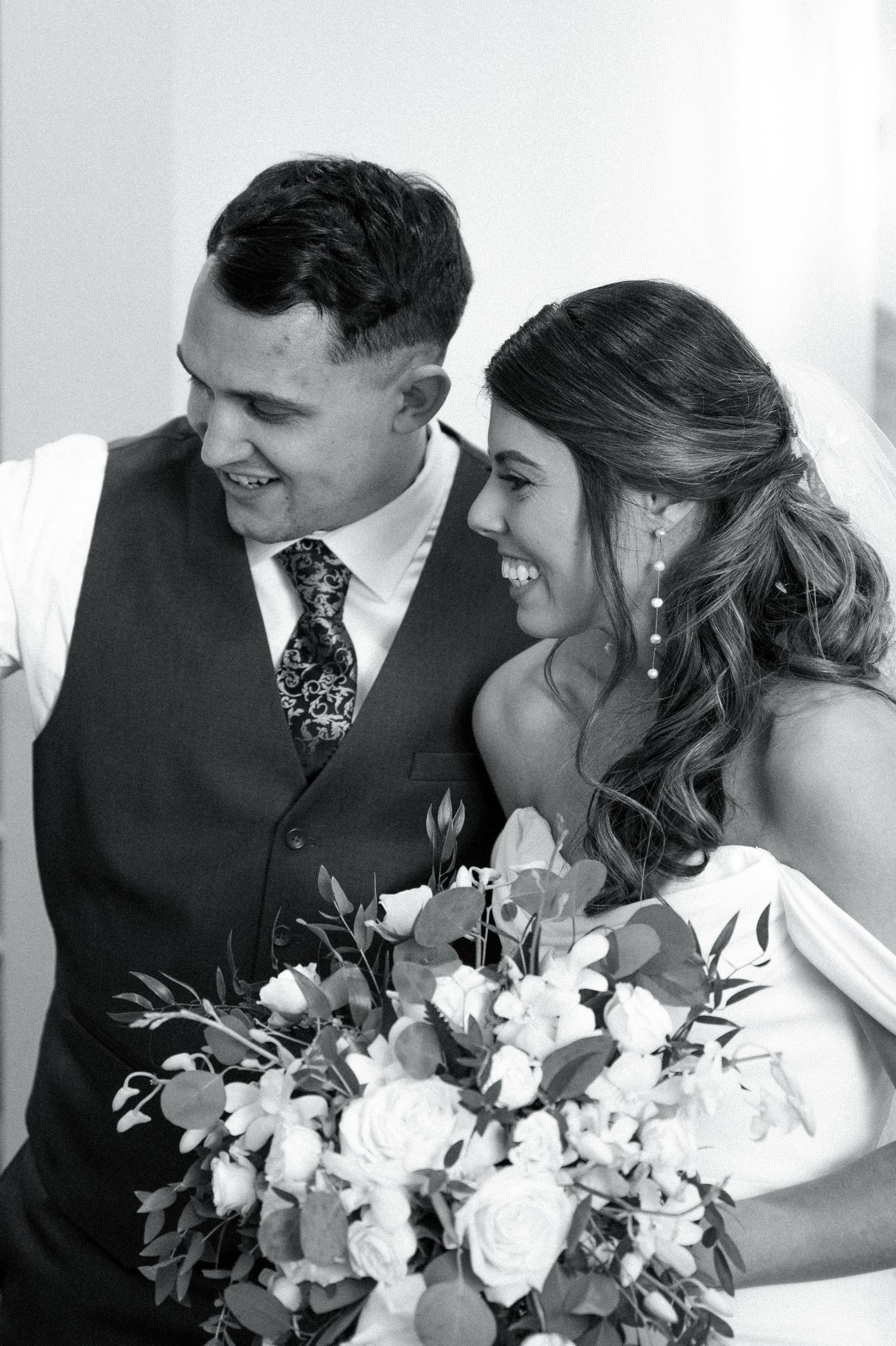 Black and white portrait of happy newlyweds with bride holding floral bouquet.