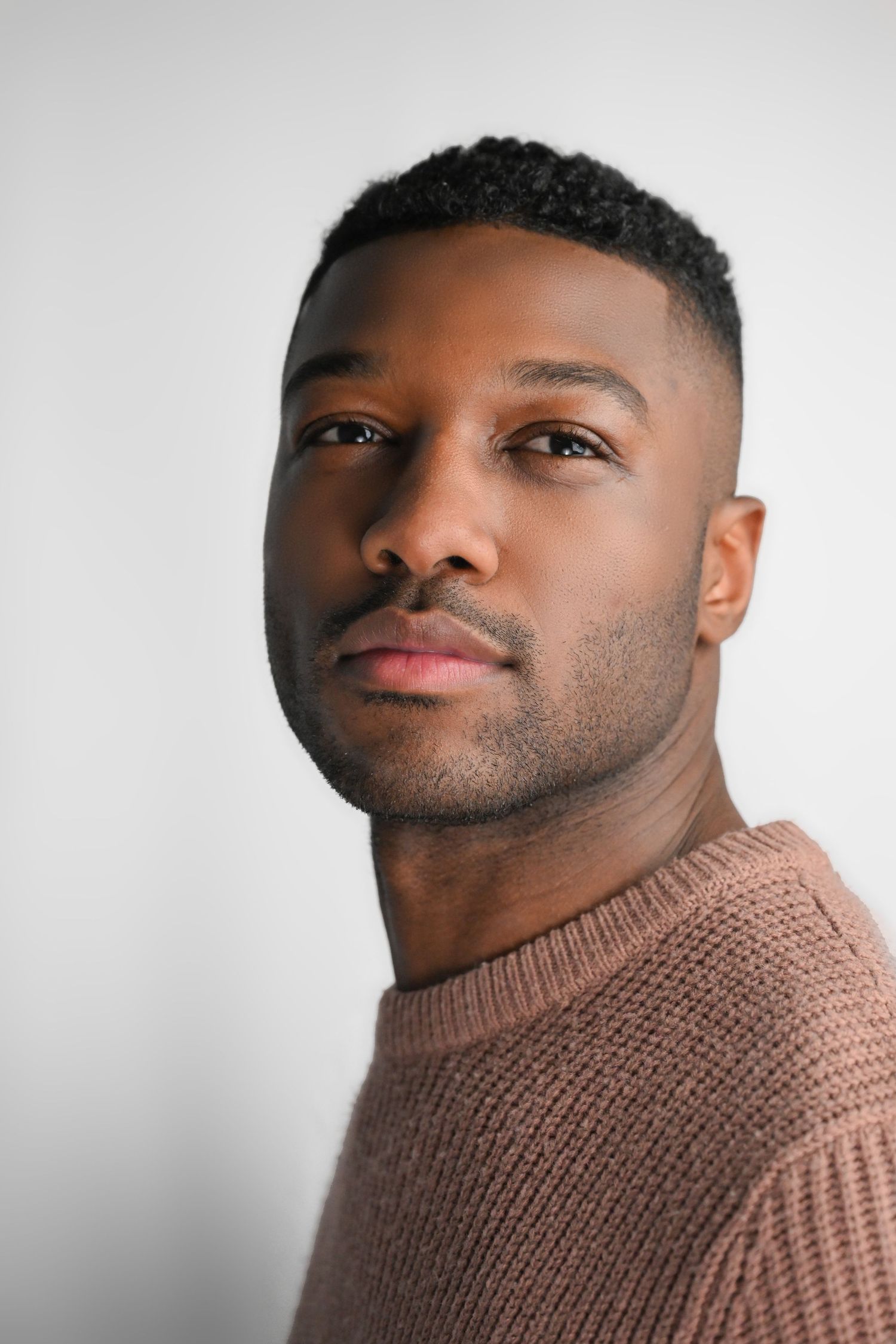 Close-up profile portraits wearing brown turtleneck sweater against white background.
