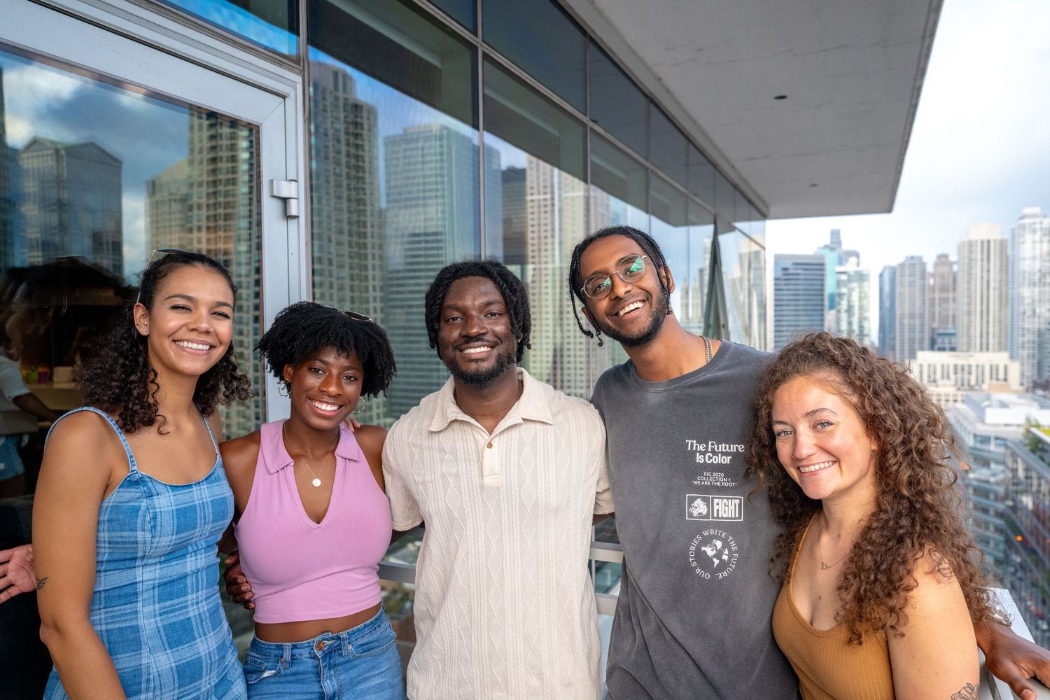 Group of friends smiling together on a balcony with city skyline in the background.