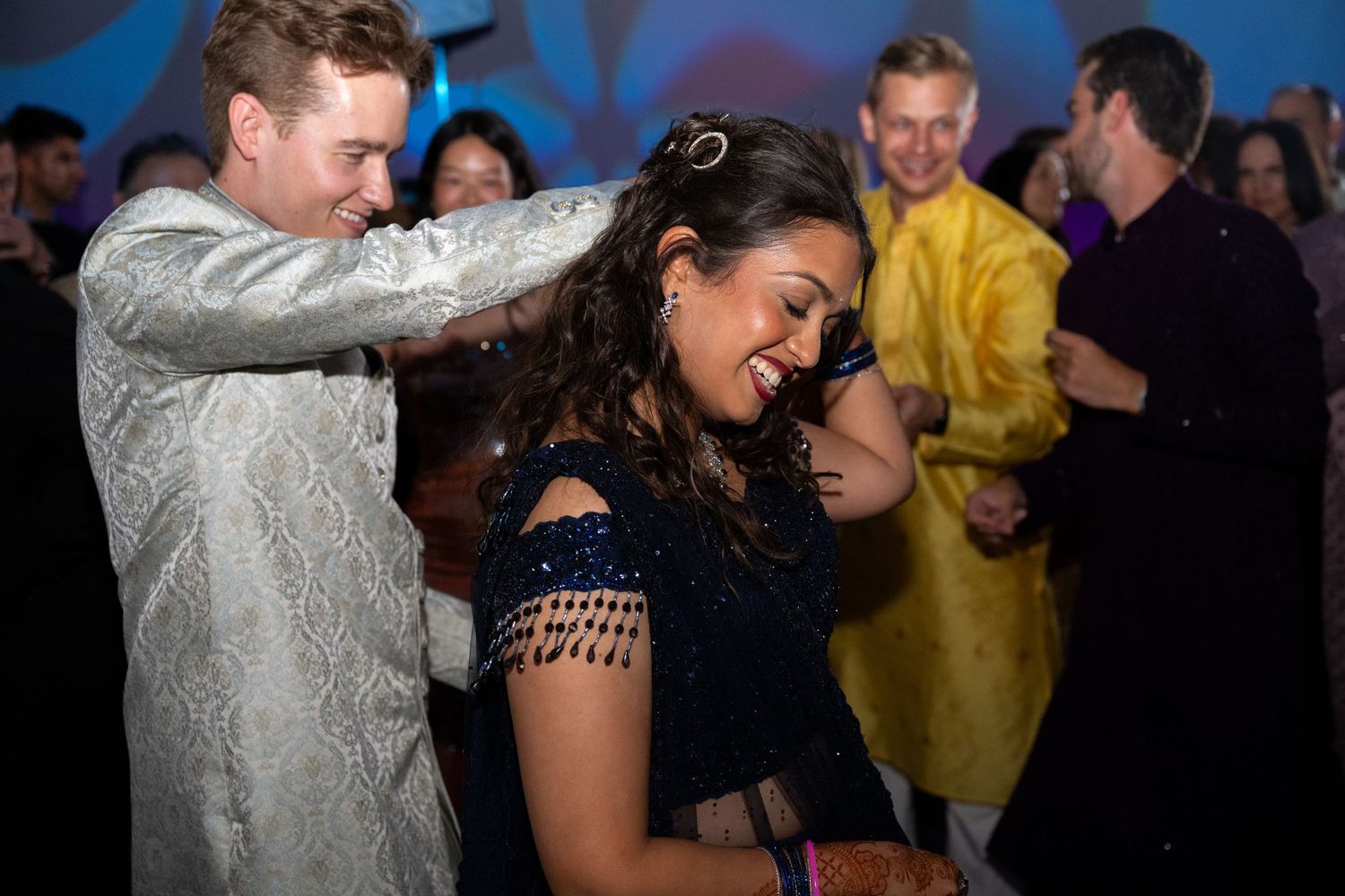 A group of people dancing and celebrating at a lively party with blue lighting in the background.