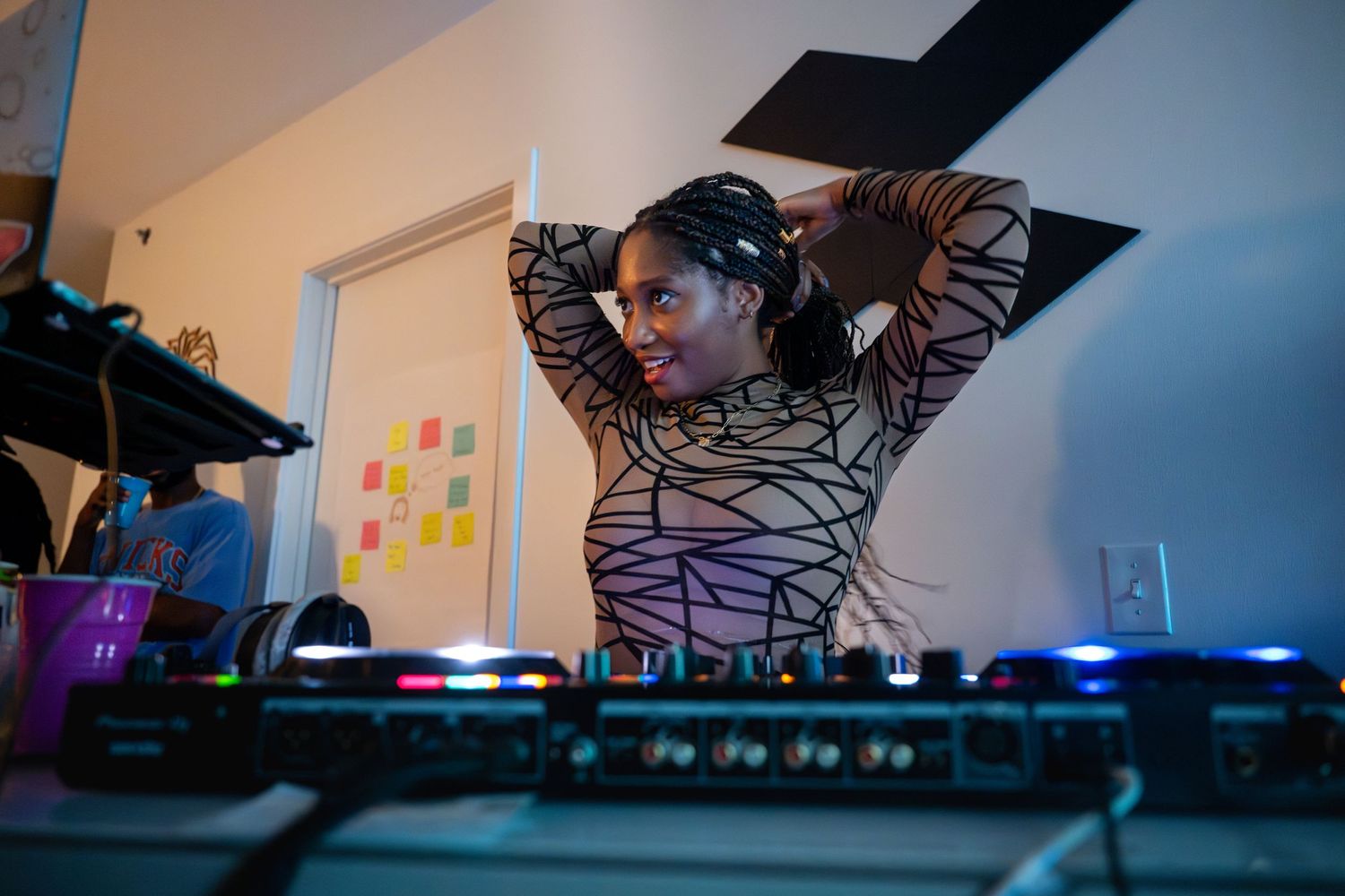 DJ working at illuminated mixing board in dimly lit room.