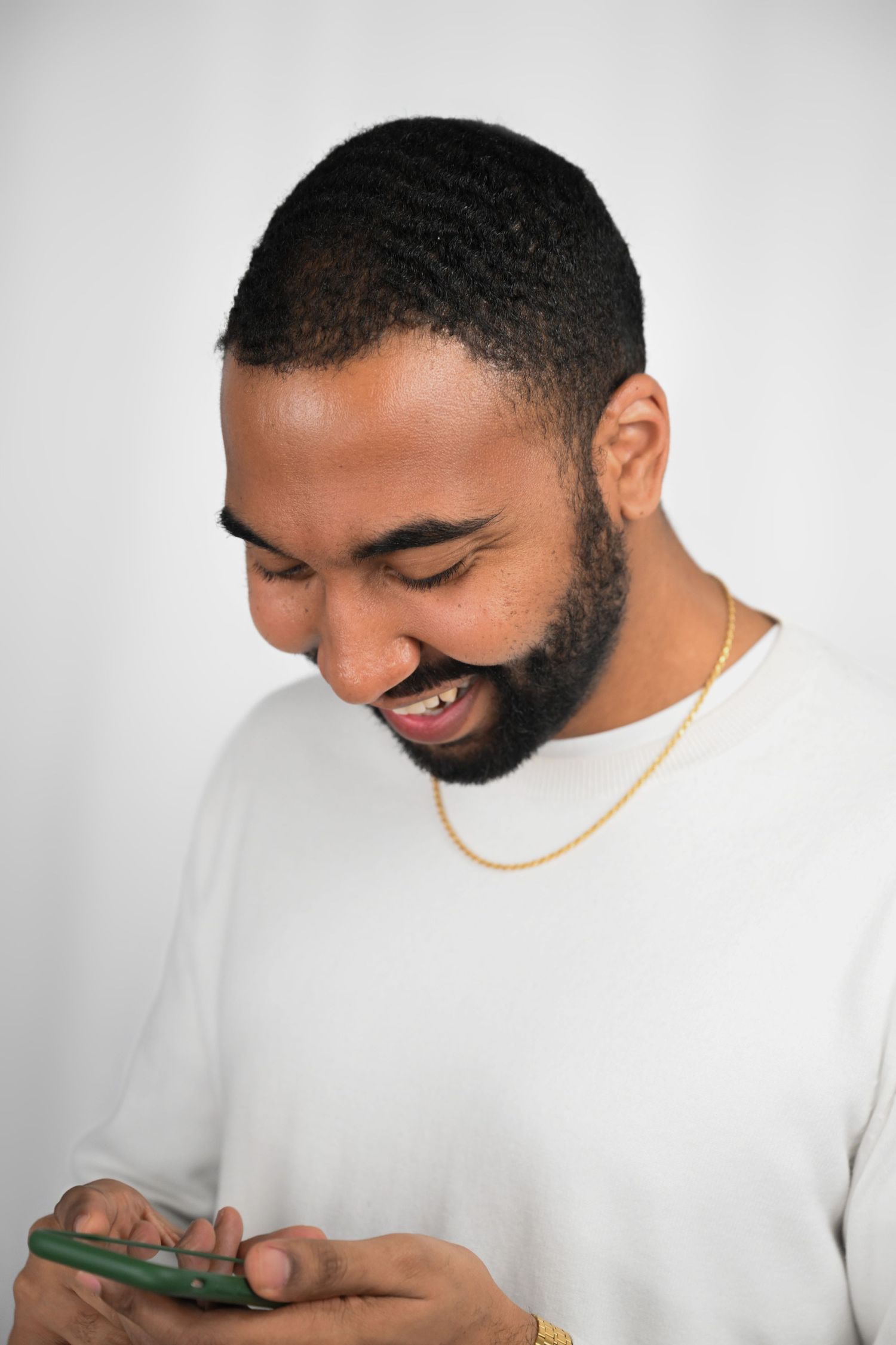 Person in white top smiling while looking at mobile phone against grey background.