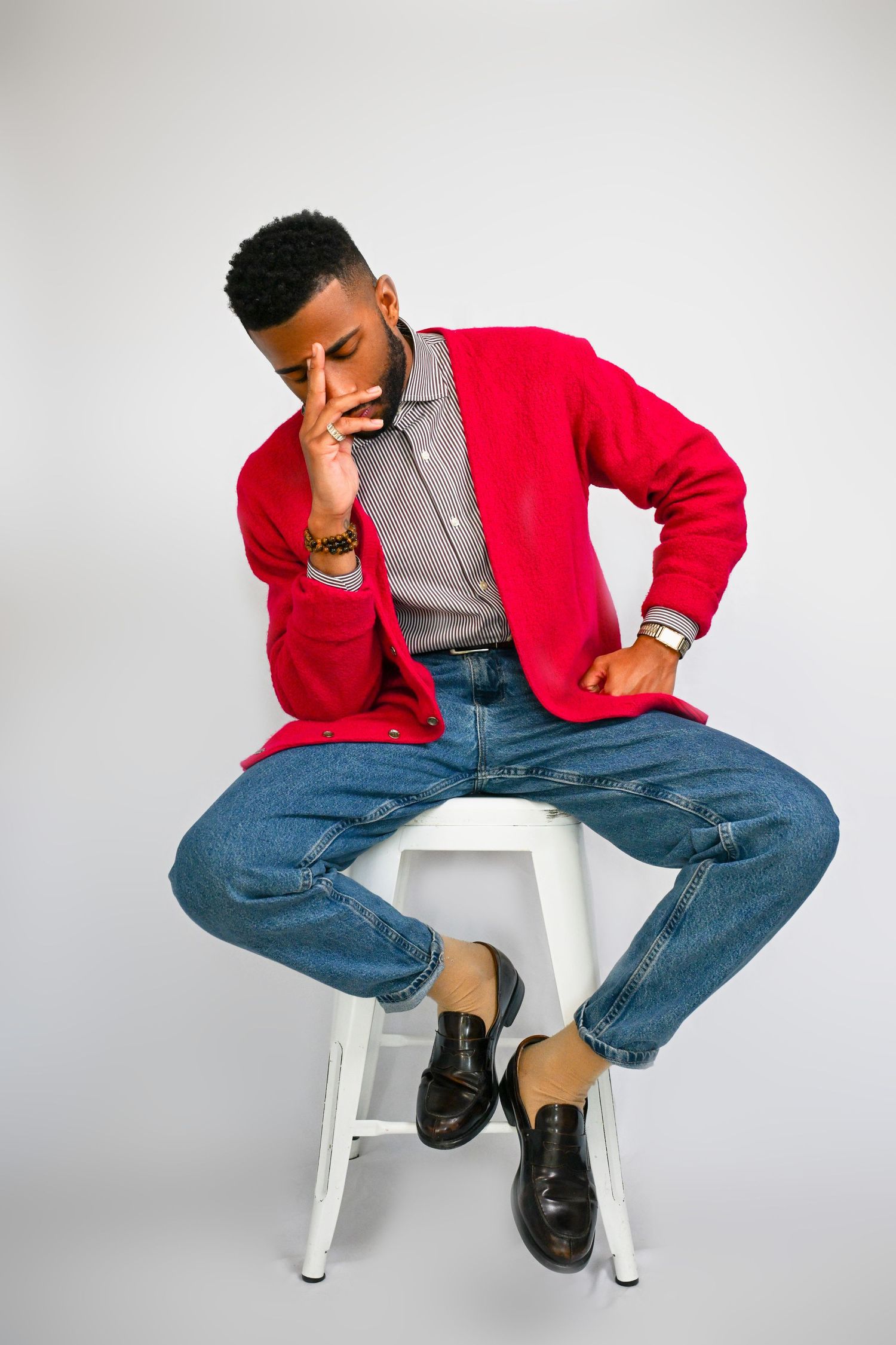 A person in a red jacket and jeans sits on a white chair in various contemplative poses against a light background.
