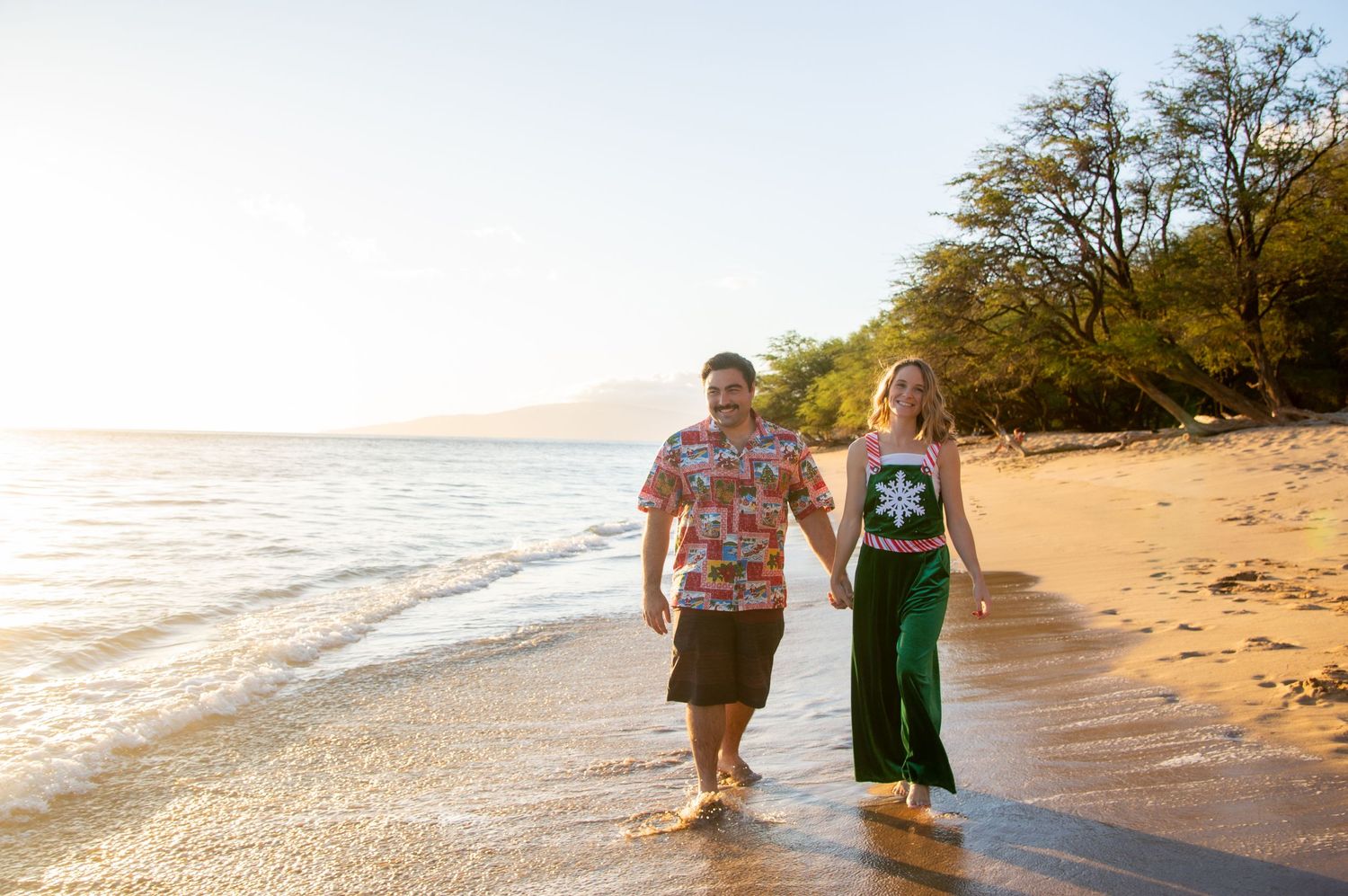 Couple walking along sandy beach at sunset wearing casual attire.