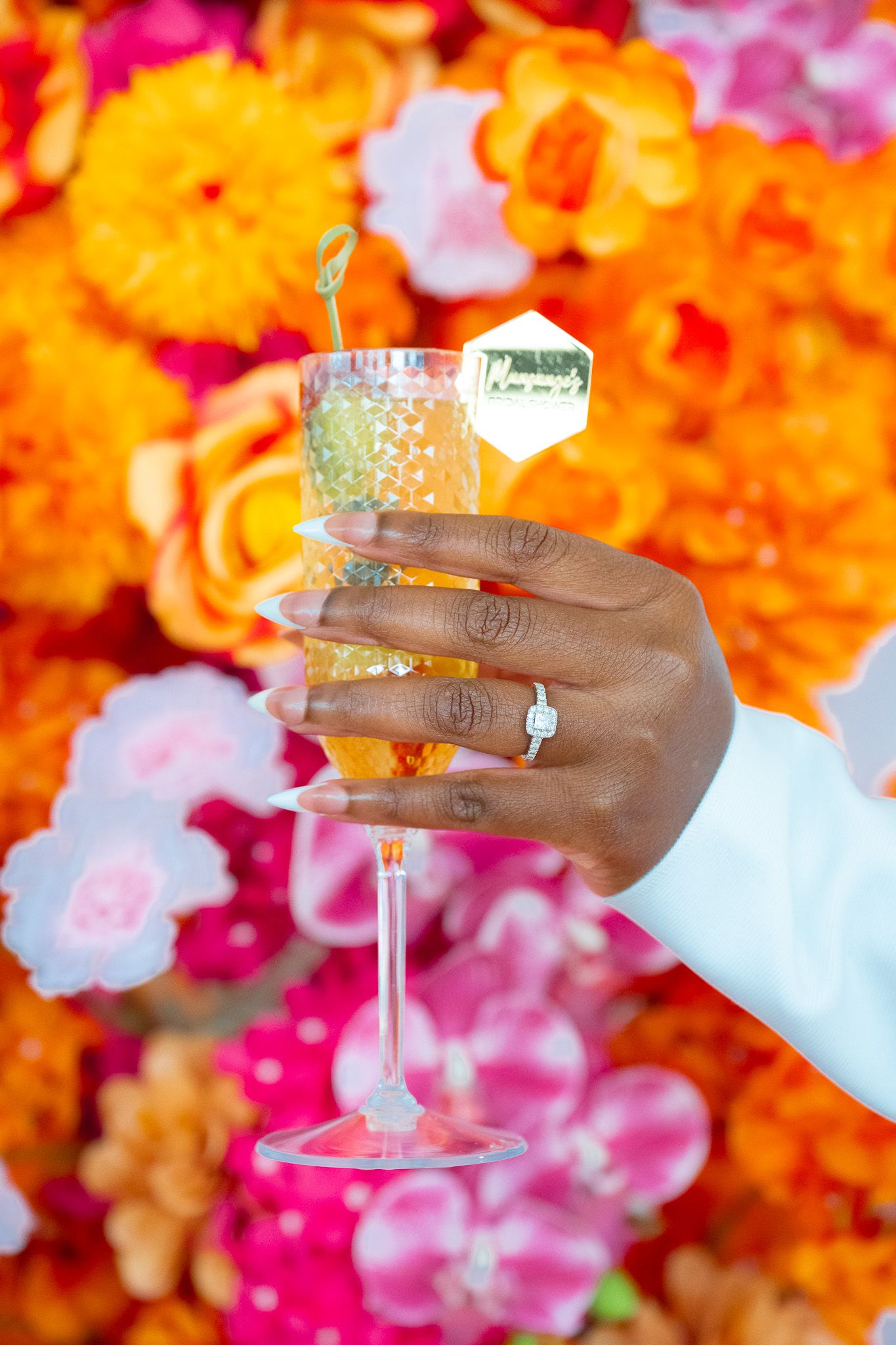 Hand holding a champagne glass with colorful floral wall backdrop.