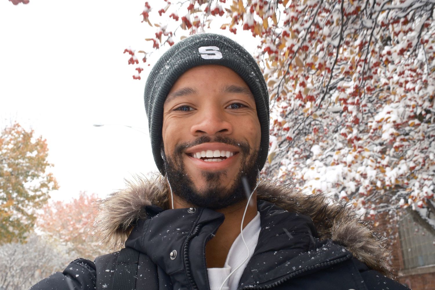 Person in winter hat smiling warmly while standing among cherry blossom trees.