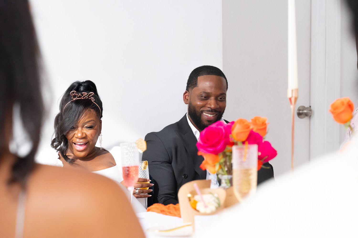 Couple seated at decorated table with champagne flutes and bright floral centerpieces.