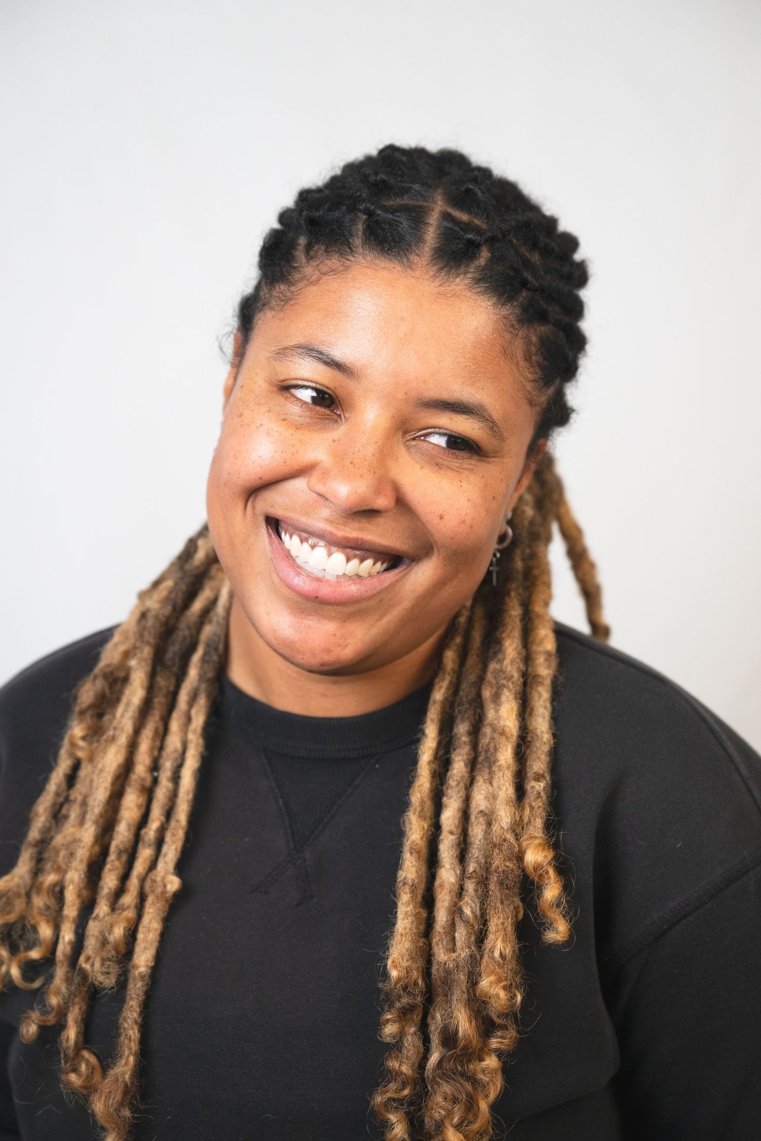 Joyful expressions of someone with blonde locs hairstyle wearing black top against white background.
