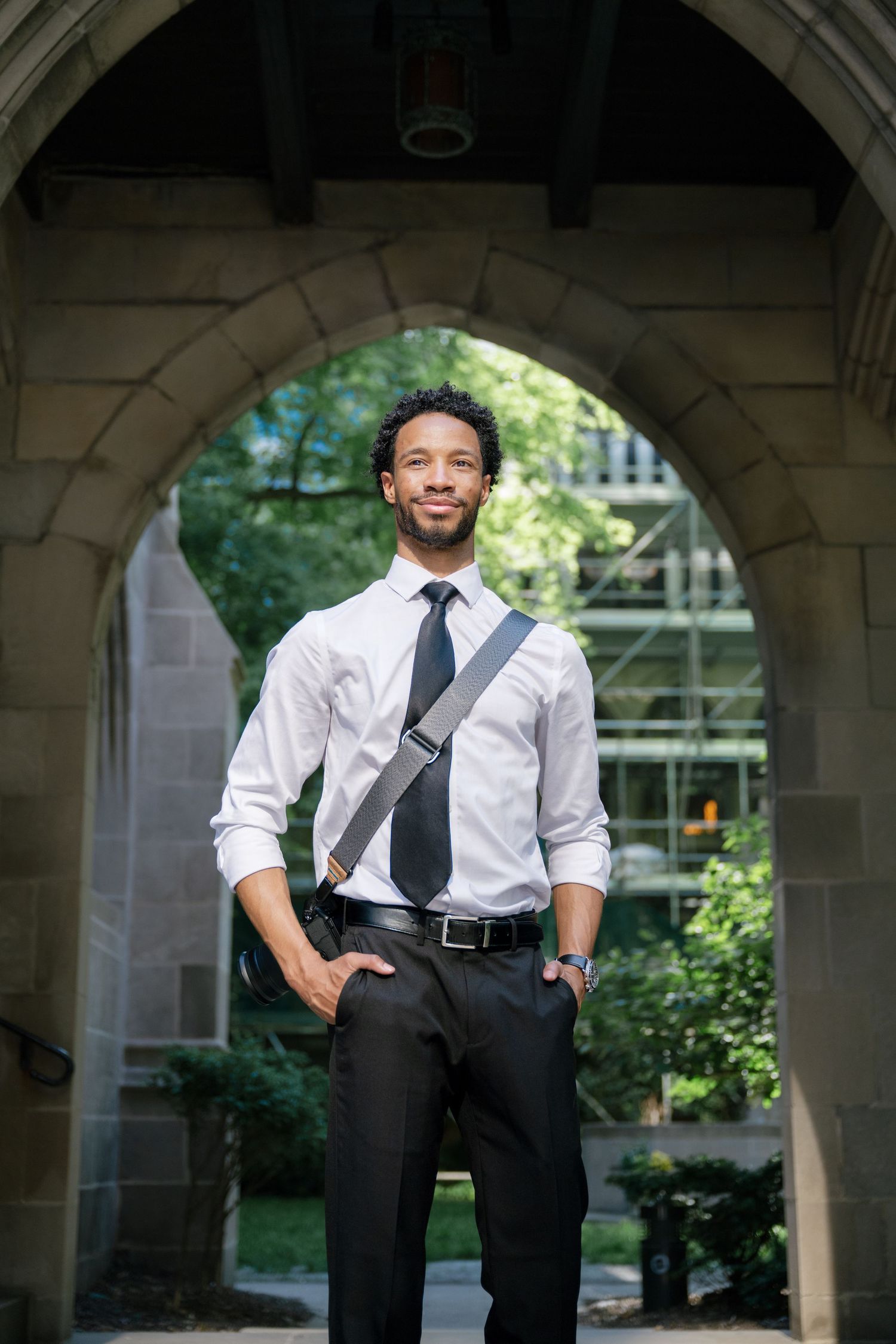 Professional wearing a white dress shirt and tie poses beneath an outdoor archway setting with natural light.