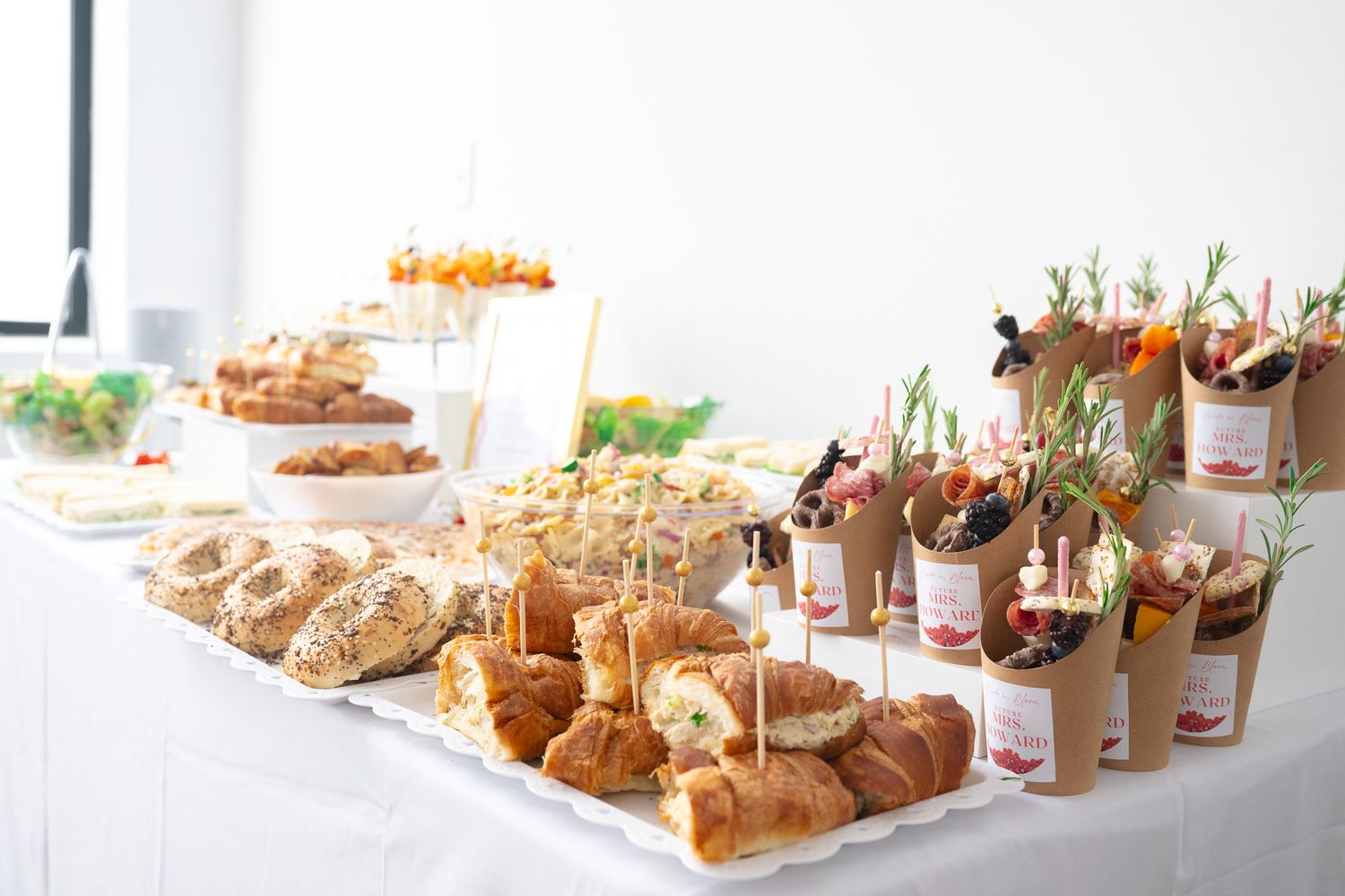 Catering table with assorted pastries, sandwiches and appetizers displayed on a white tablecloth.