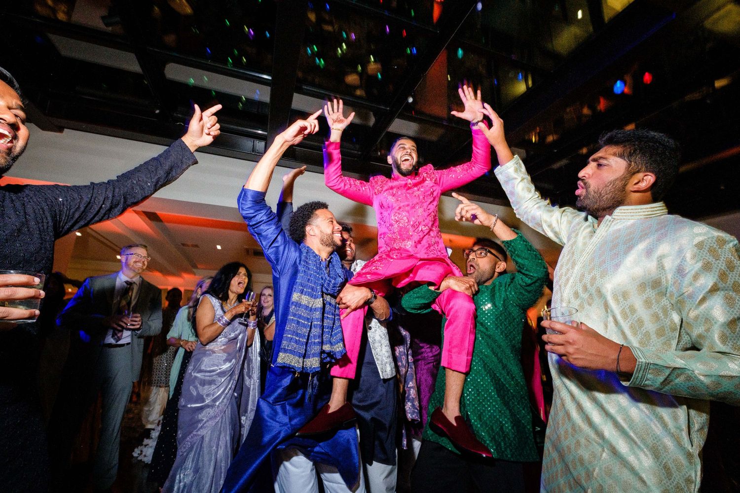 Energetic crowd dancing and celebrating at a party with colorful lighting.