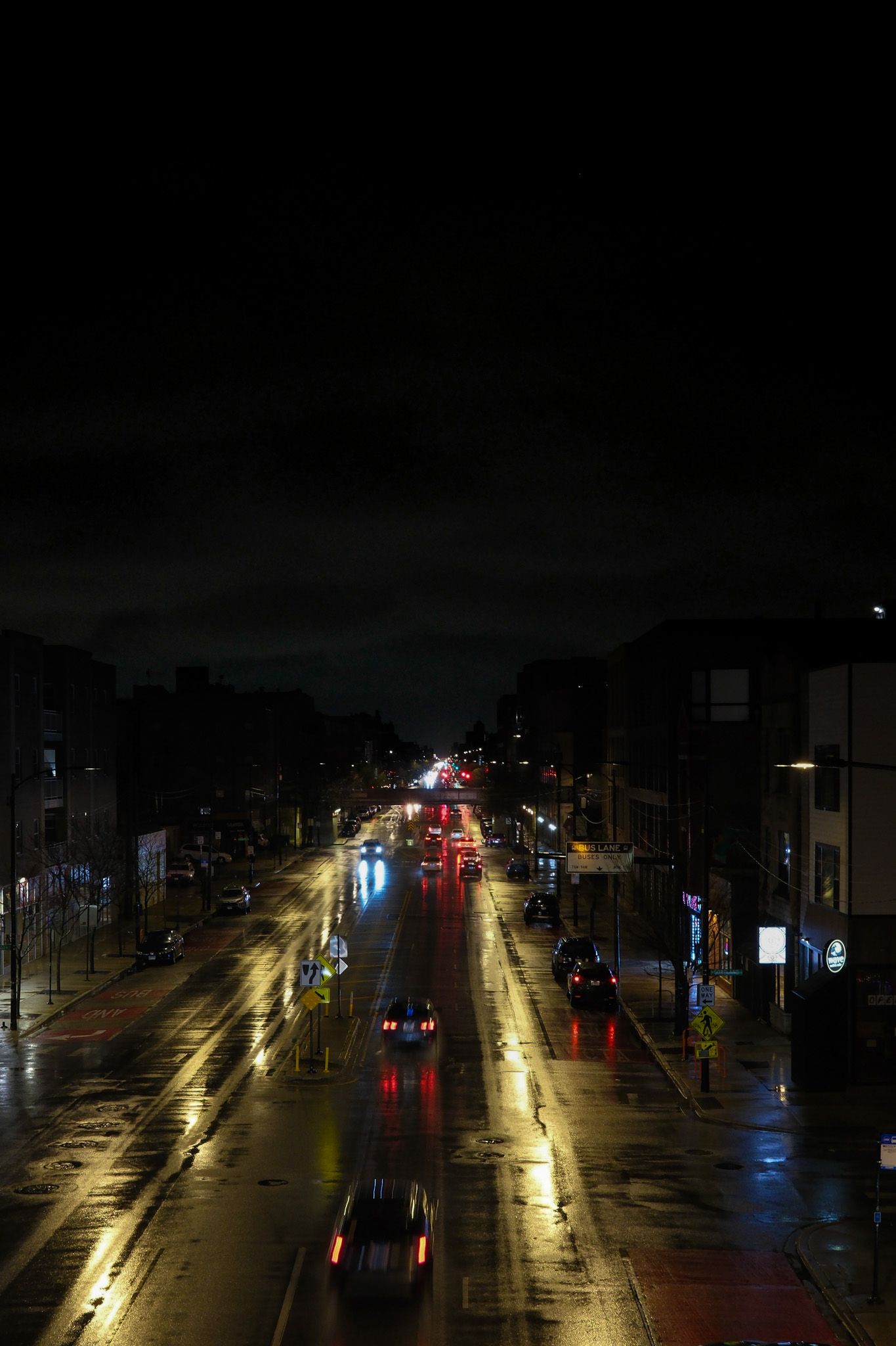 Rainy night street scene with car headlights reflecting off wet pavement.