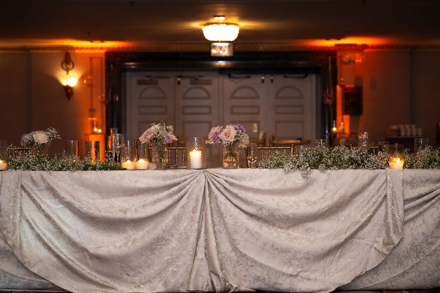 An elegant wedding reception venue with white draped tables and warm ambient lighting creating a romantic atmosphere.