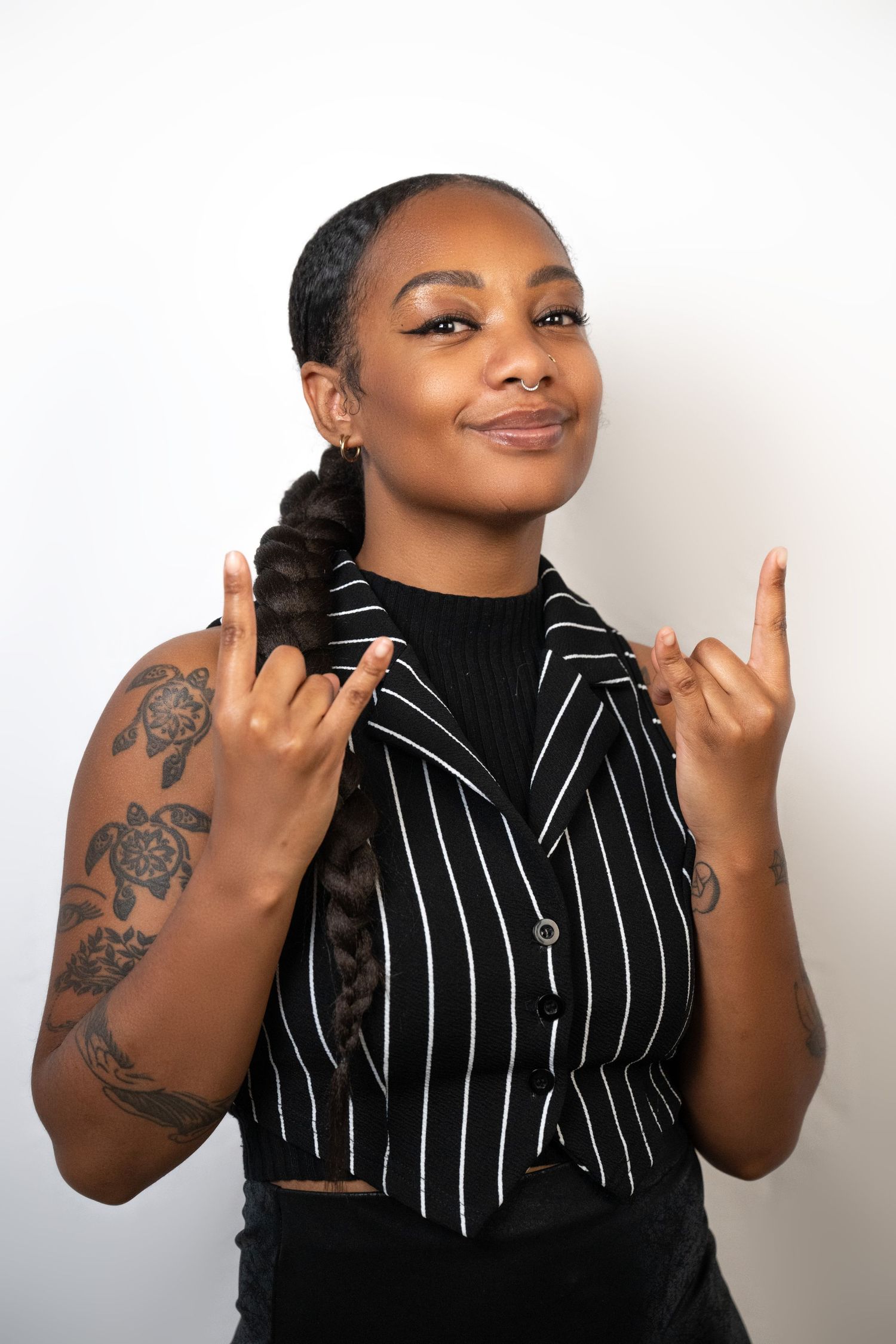 Person in striped top with tattoos making hand gestures against white background.