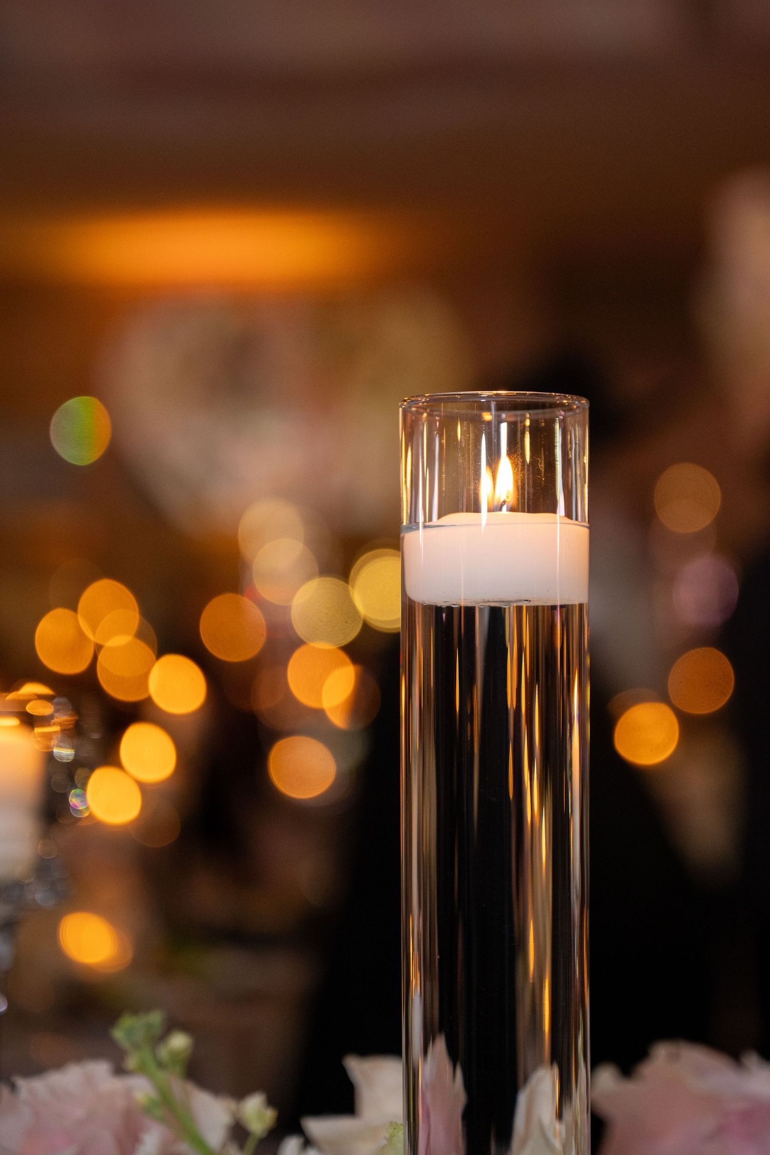Elegant floating candles in tall glass cylinders create a romantic ambiance with blurred golden bokeh lights in the background.