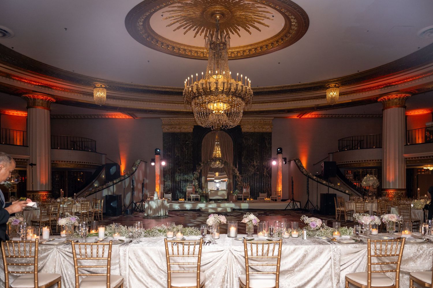 Panoramic view of an elegant ballroom with crystal chandeliers and white chair covers set for a formal wedding reception.