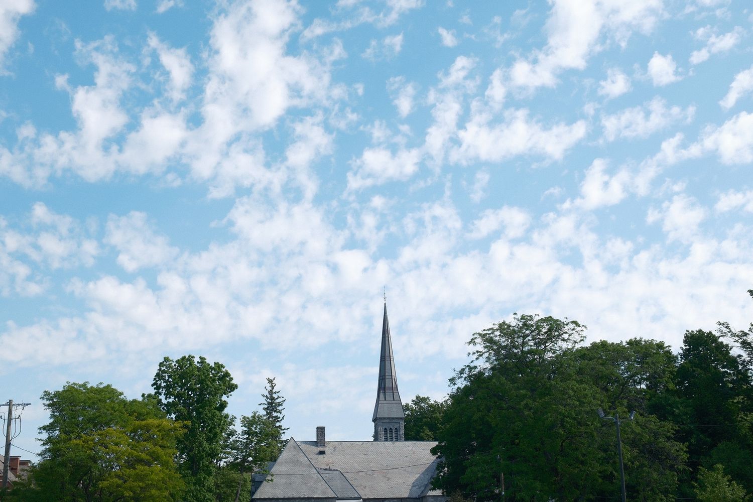 Church spire piercing a bright blue sky dotted with puffy white clouds.