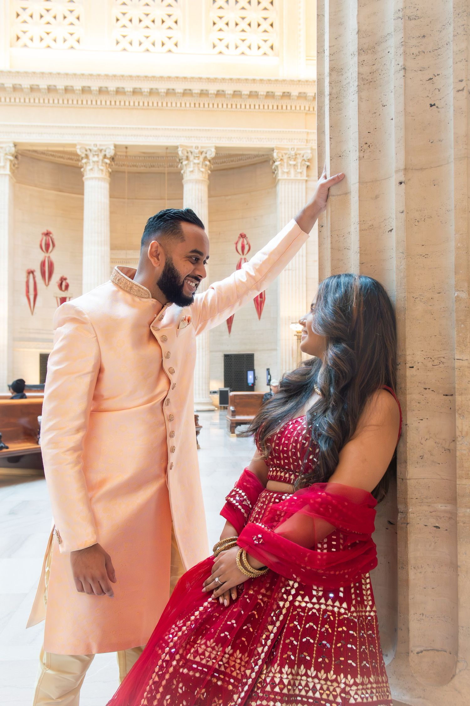 Couple in traditional Indian wedding attire dancing between ornate marble columns.