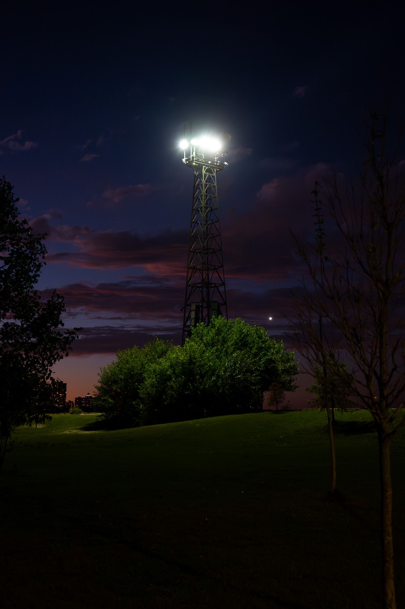 Illuminated cell tower against purple twilight sky on grassy hill.