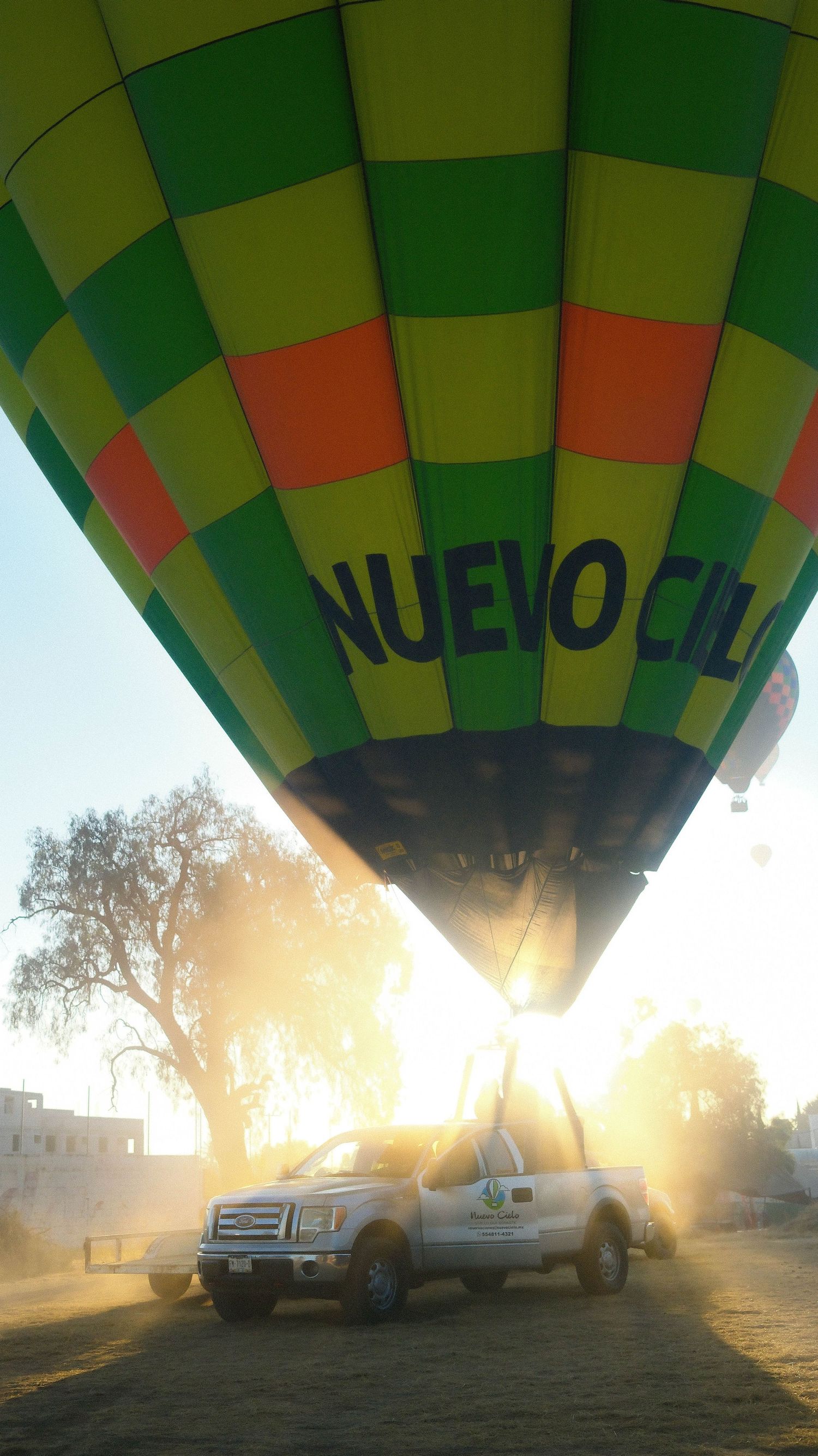 Hot air balloon crew prepares for launch at sunrise with trucks and equipment silhouetted in the morning mist.