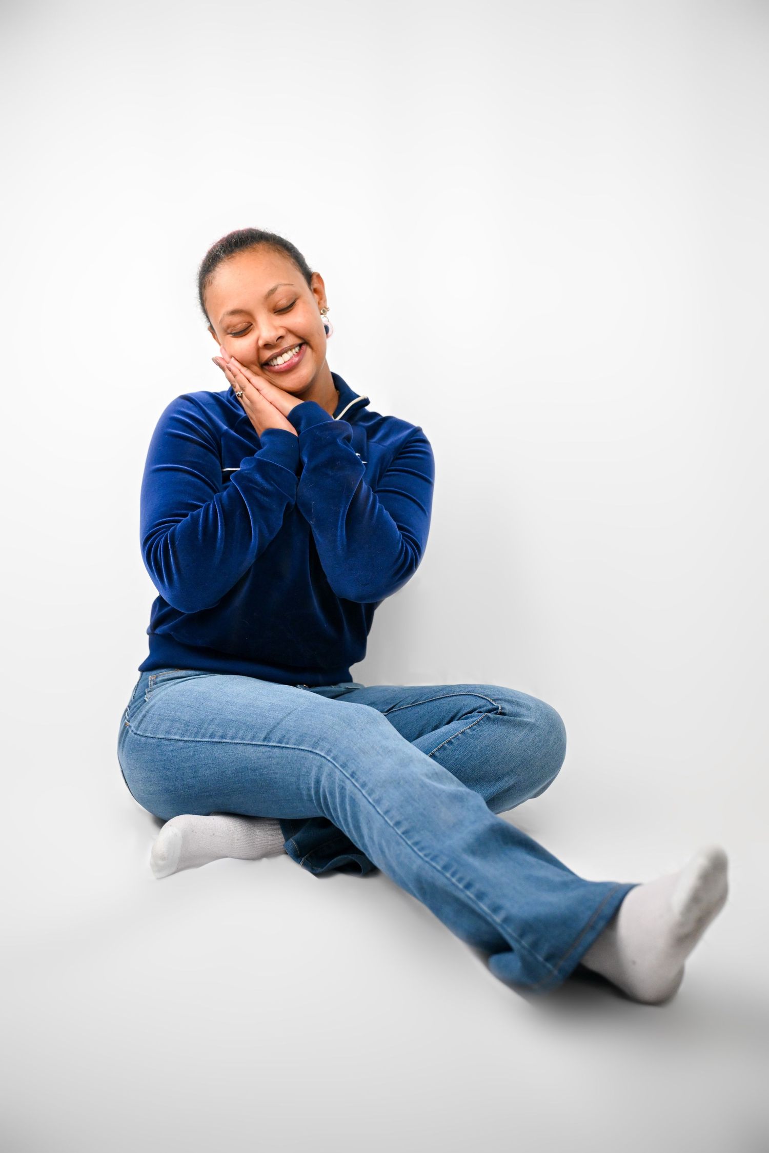 Casual portrait in blue sweater and jeans sitting on white background.