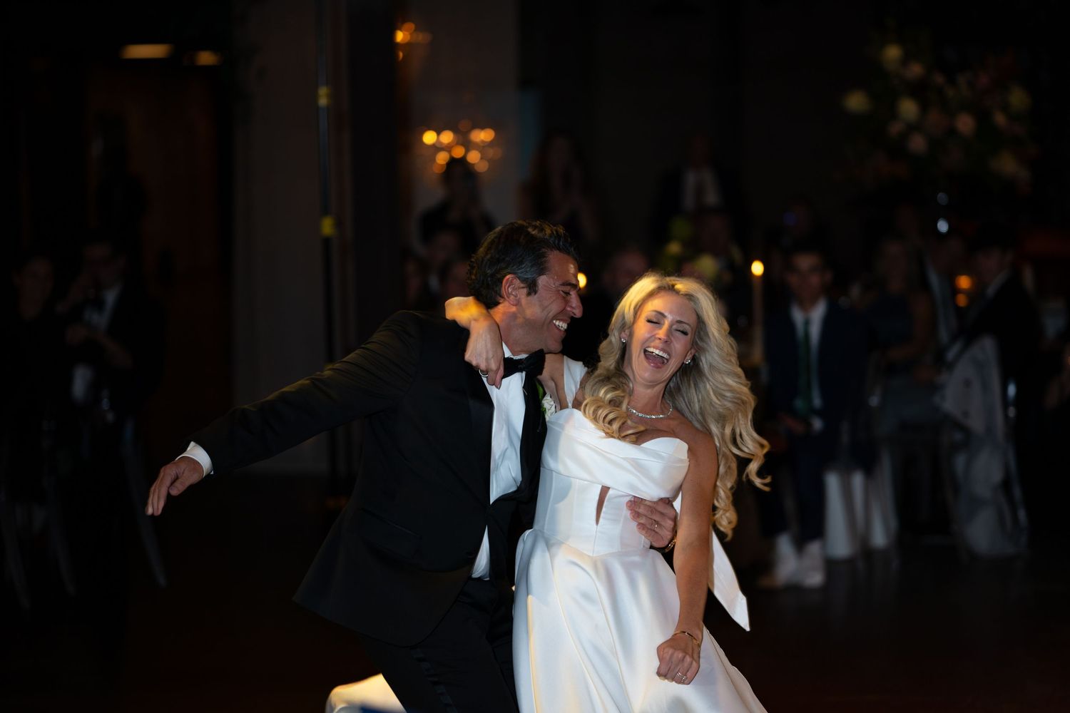 A couple shares their first dance at a wedding reception in a dimly lit ballroom with romantic lighting.