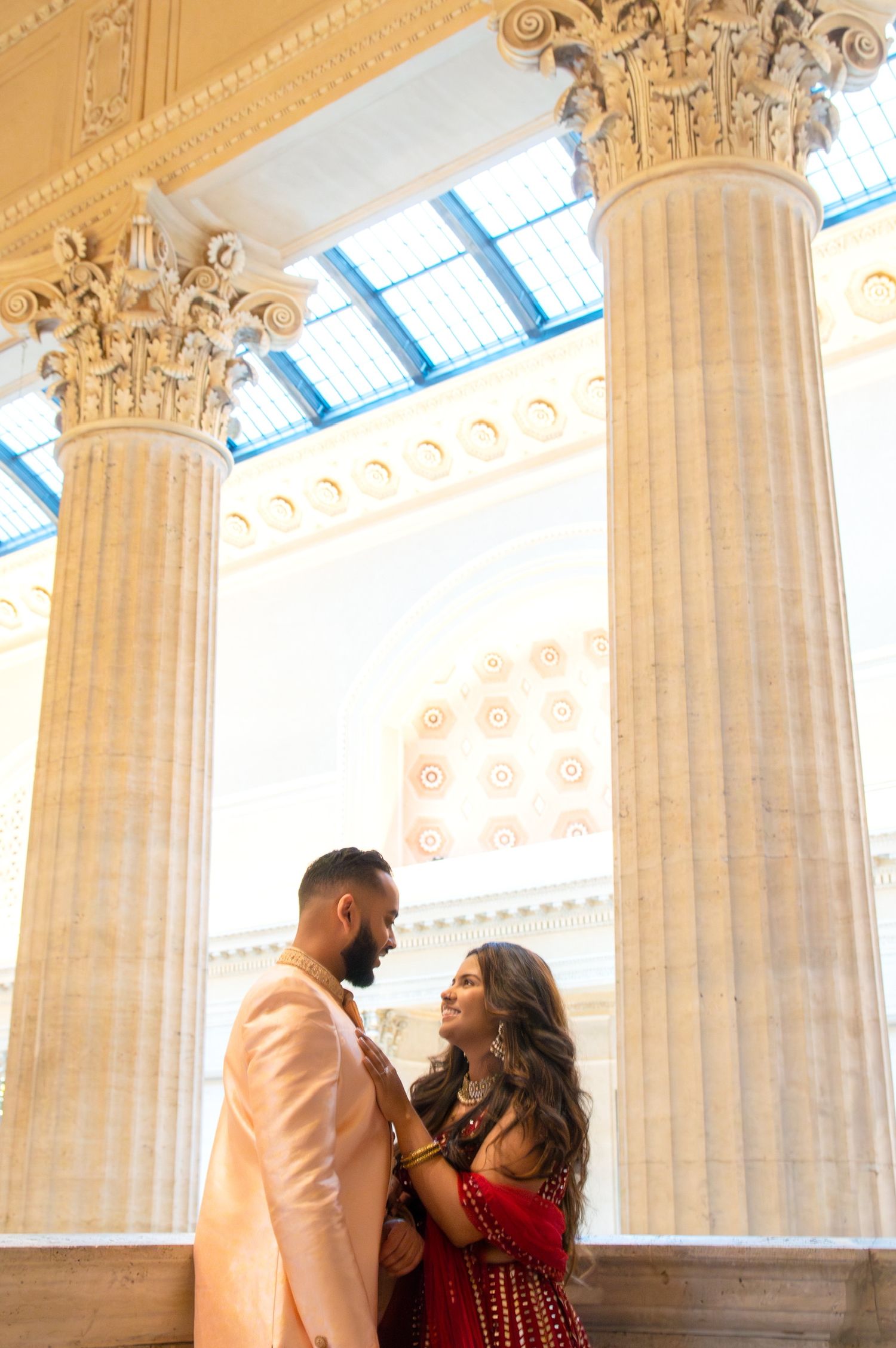 Romantic moment between couple framed by grand architectural columns and skylight.
