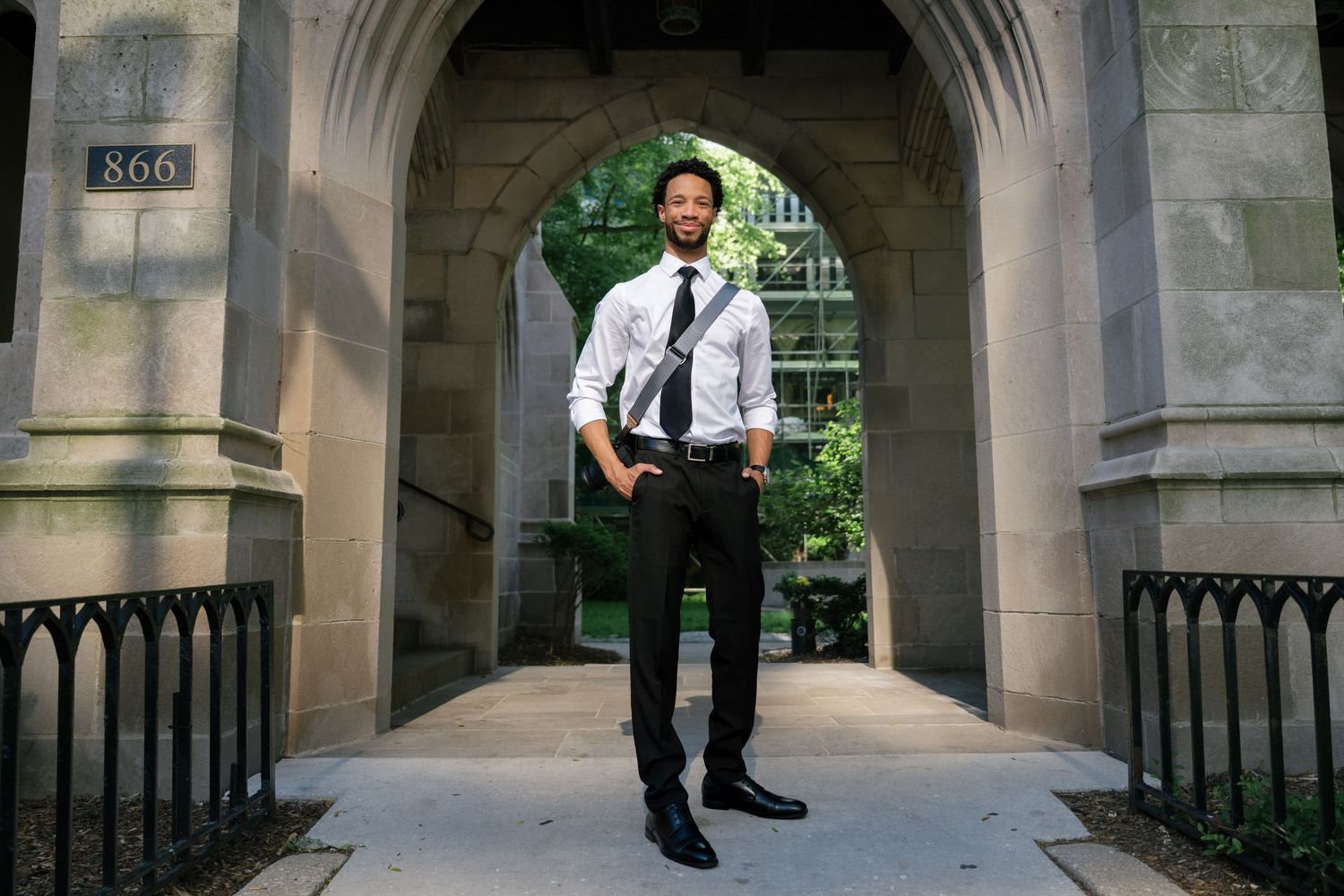 A person in professional attire walks through an elegant stone archway corridor at a university building.