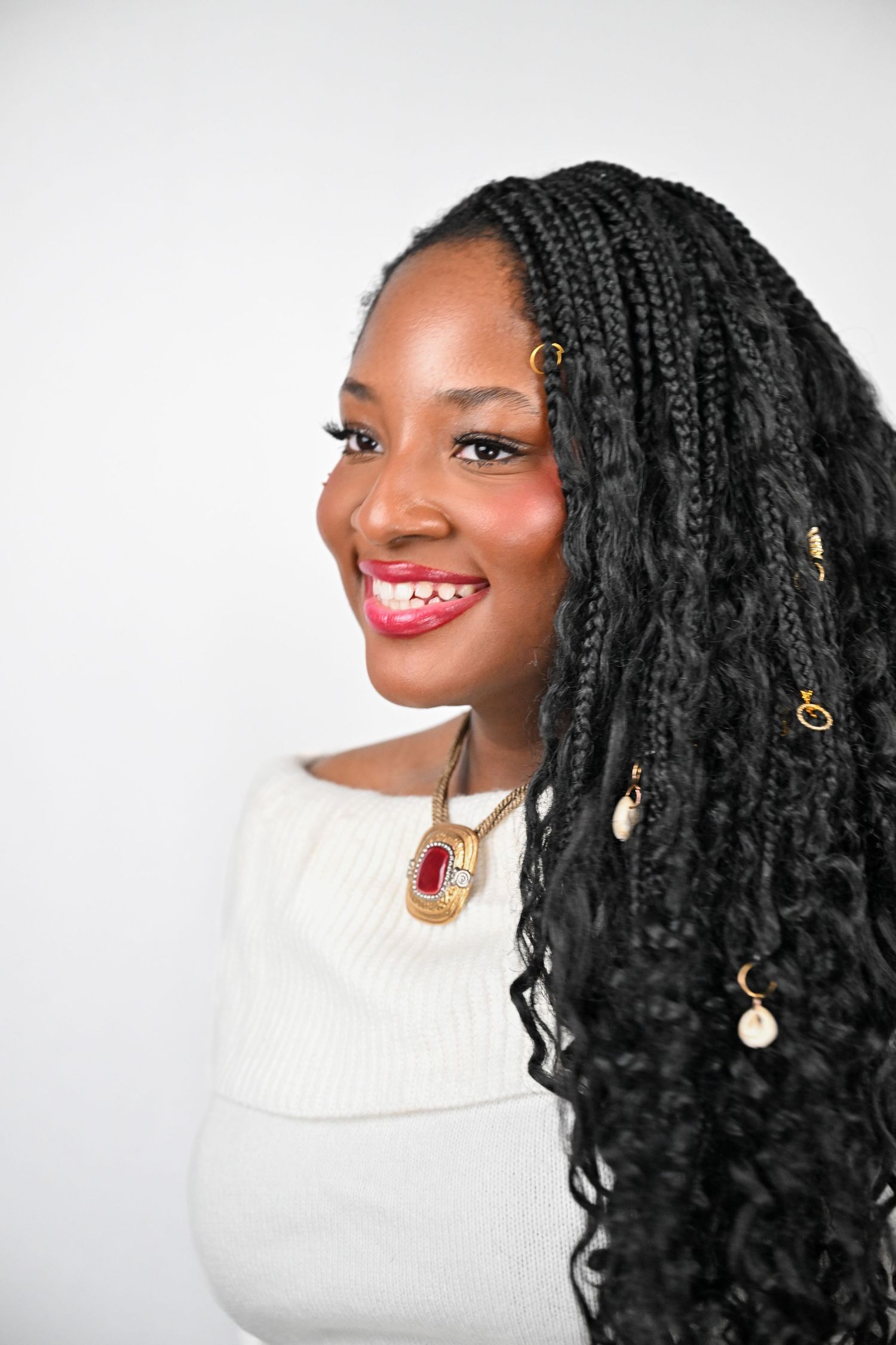 Portrait series of a person with voluminous black braids wearing a white turtleneck sweater and gold earrings.