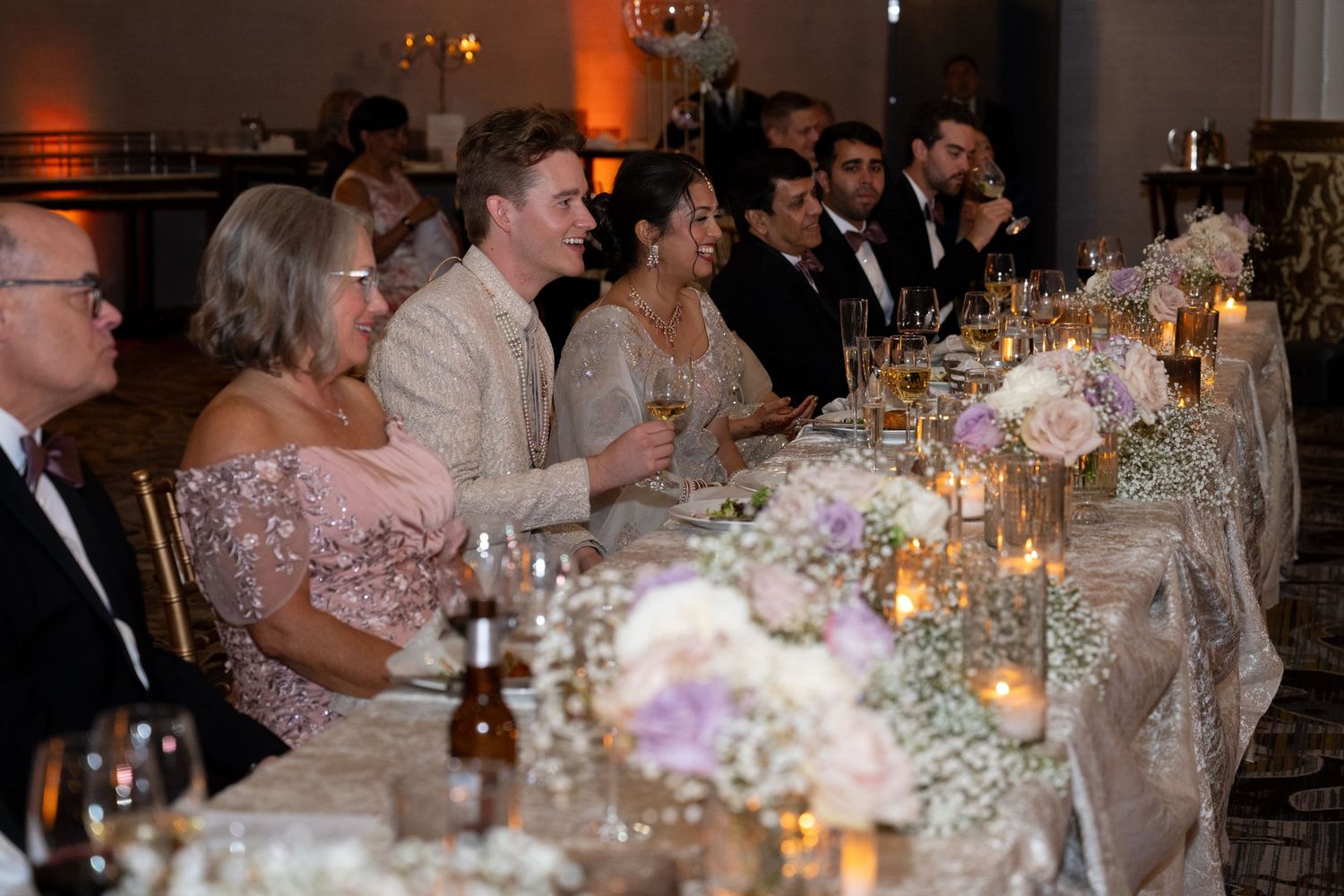 Wedding reception guests seated at elegant tables with candlelight and white floral centerpieces in a formal dining room.