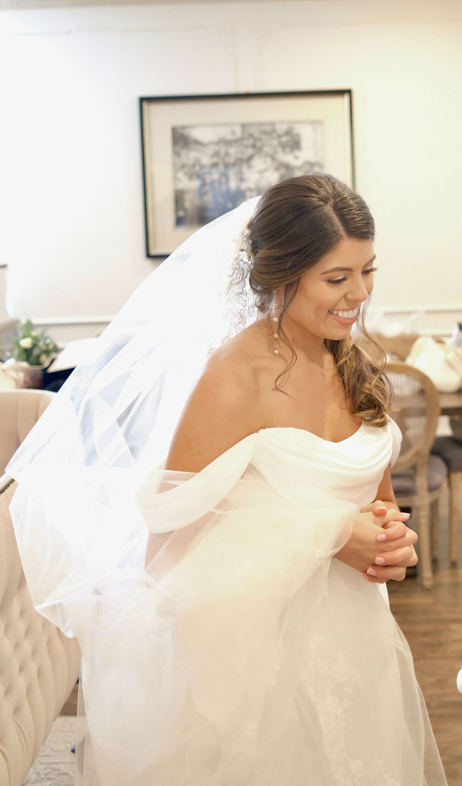 A bride in a white strapless gown and veil stands glowing with joy.