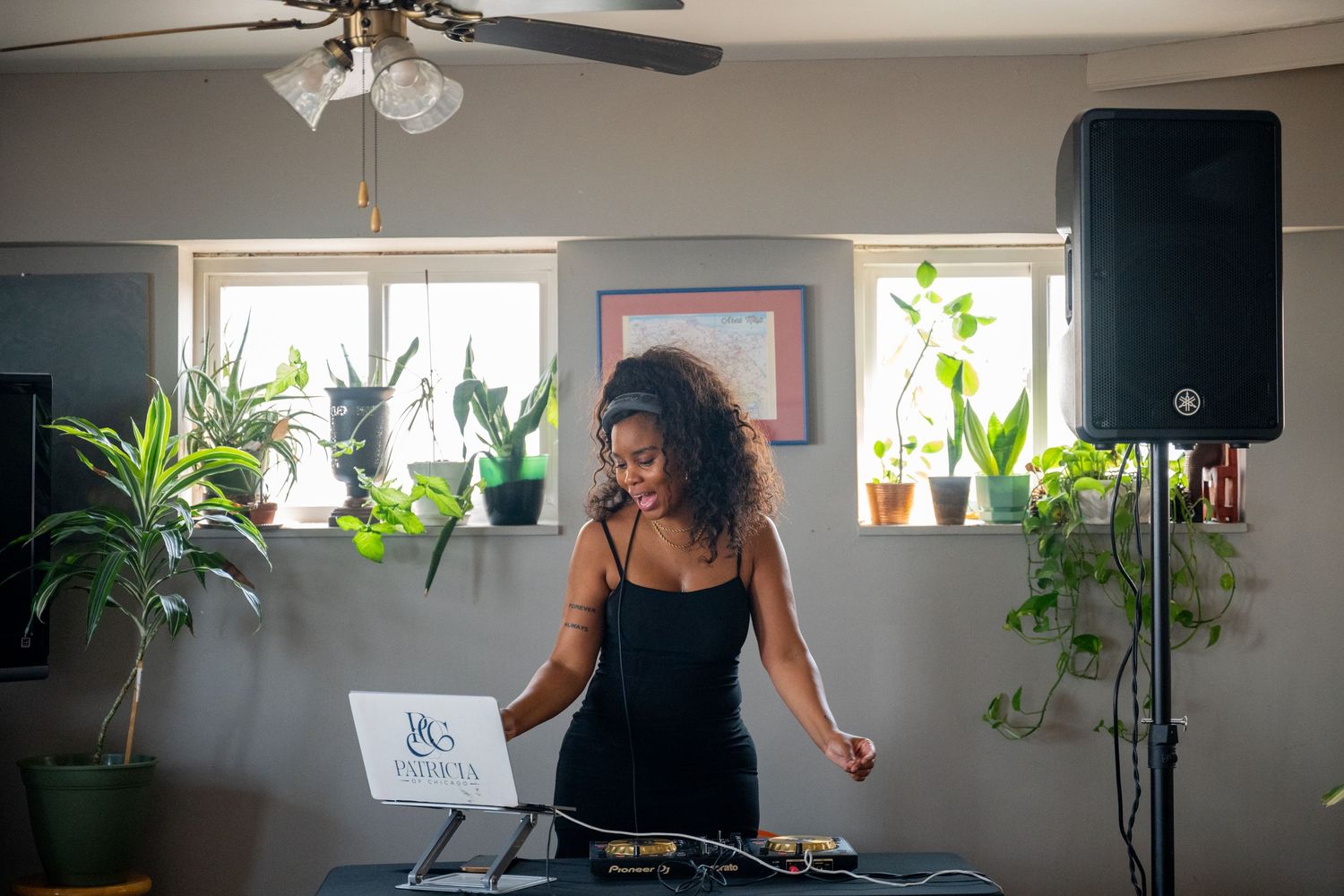 DJ setup in bright room with plants and ceiling fan visible.